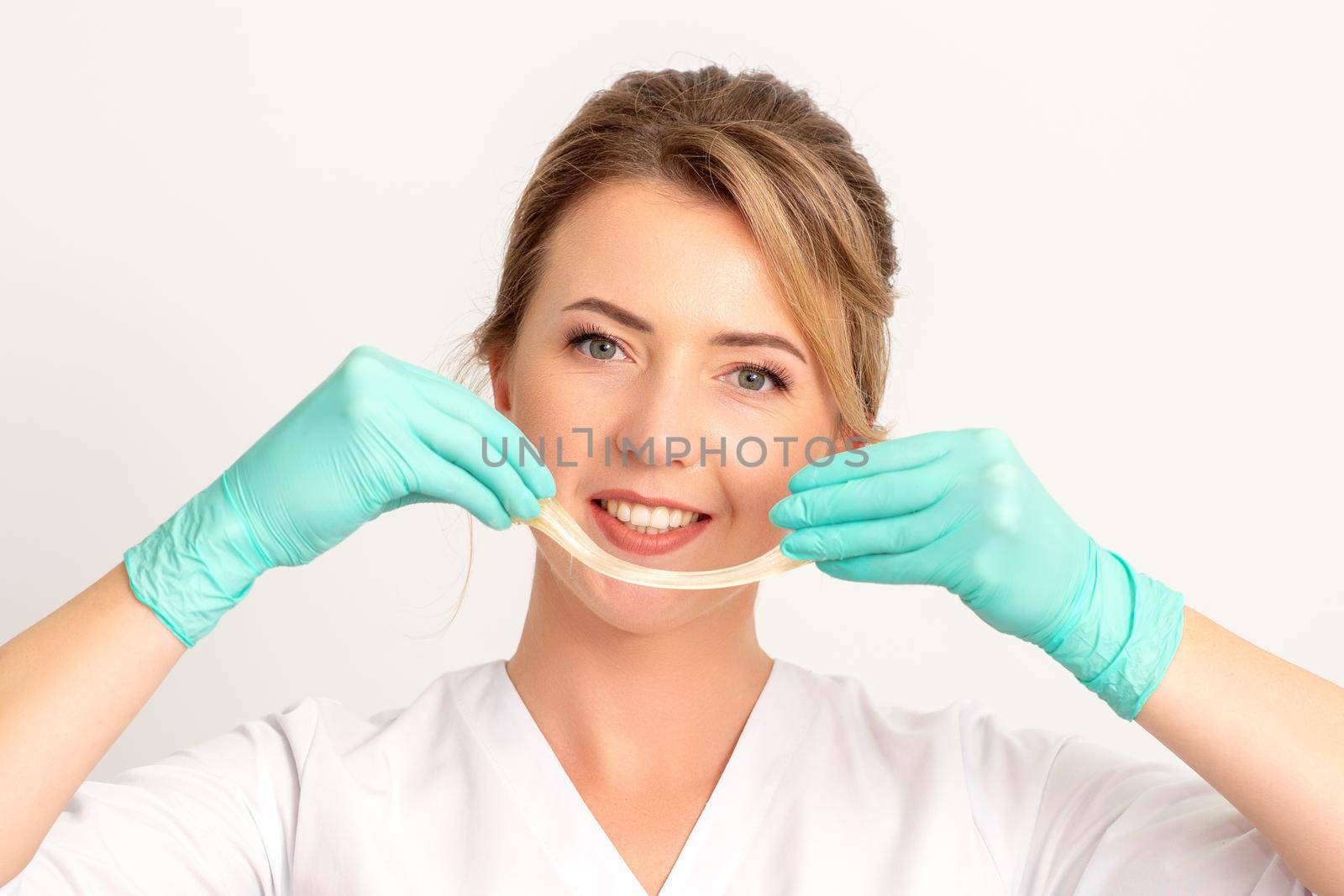 Young caucasian smiling female beautician holding wax for depilation over white background. Yellow sugar paste in hands master of depilation. Epilation concept
