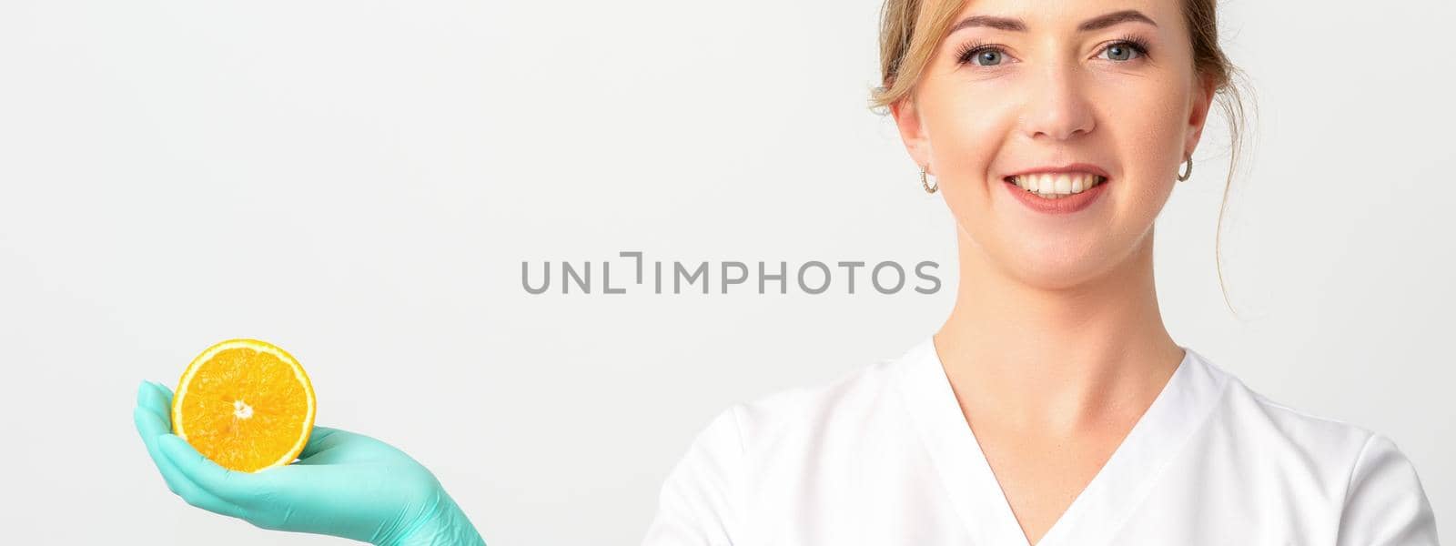 Smiling female nutritionist holding a sliced orange, looking at camera over white background, healthy diet concept