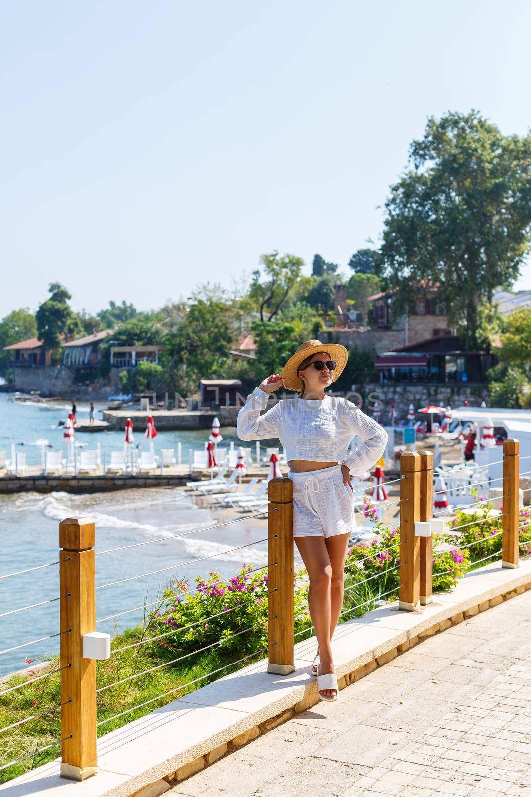 A young slender tanned woman in white shorts and a T-shirt, wearing sunglasses and a hat. Walk on a hot sunny day in the ancient city