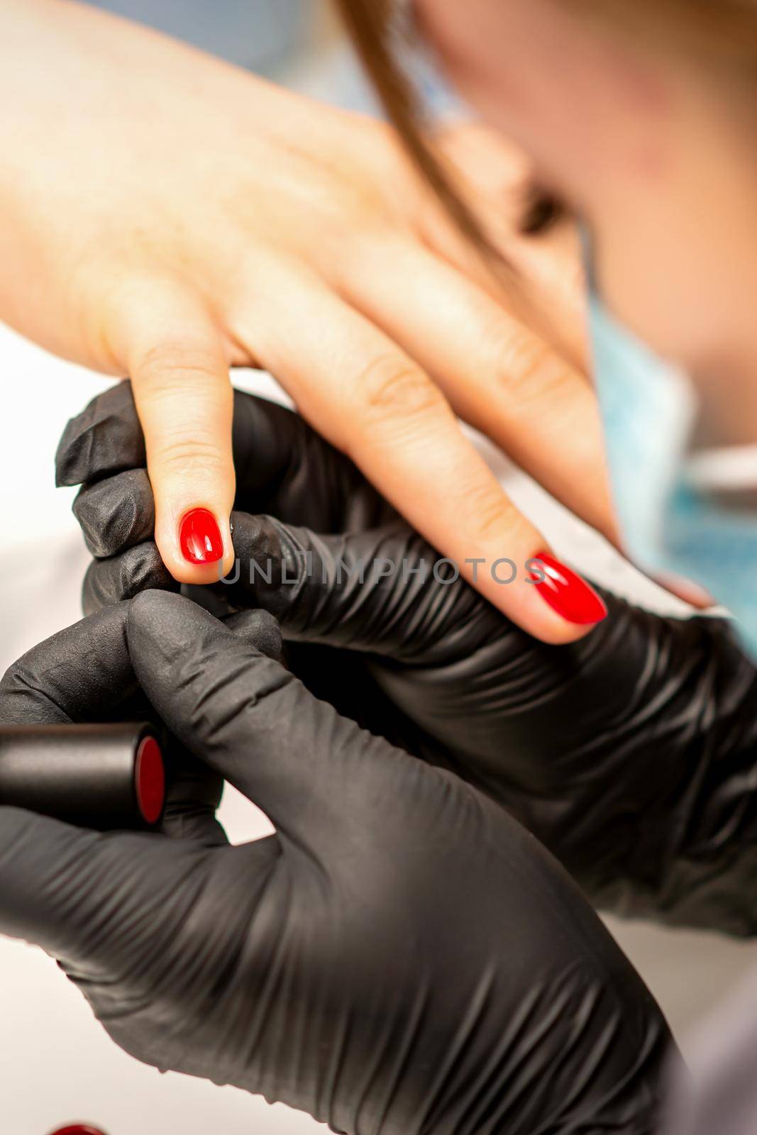 Manicure varnish painting. Close-up of a manicure master wearing rubber black gloves applying red varnish on a female fingernail in the beauty salon