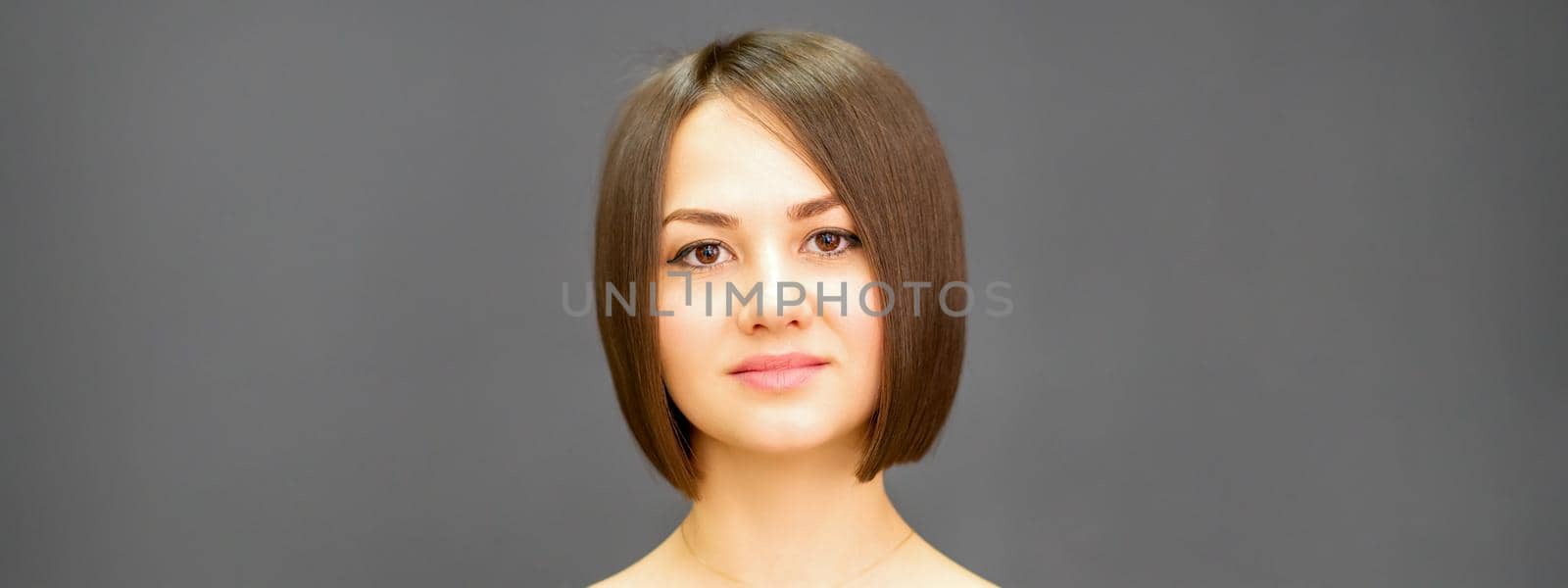 Beautiful young caucasian brunette woman with short hairstyle smiling and looking at camera against dark gray background with copy space