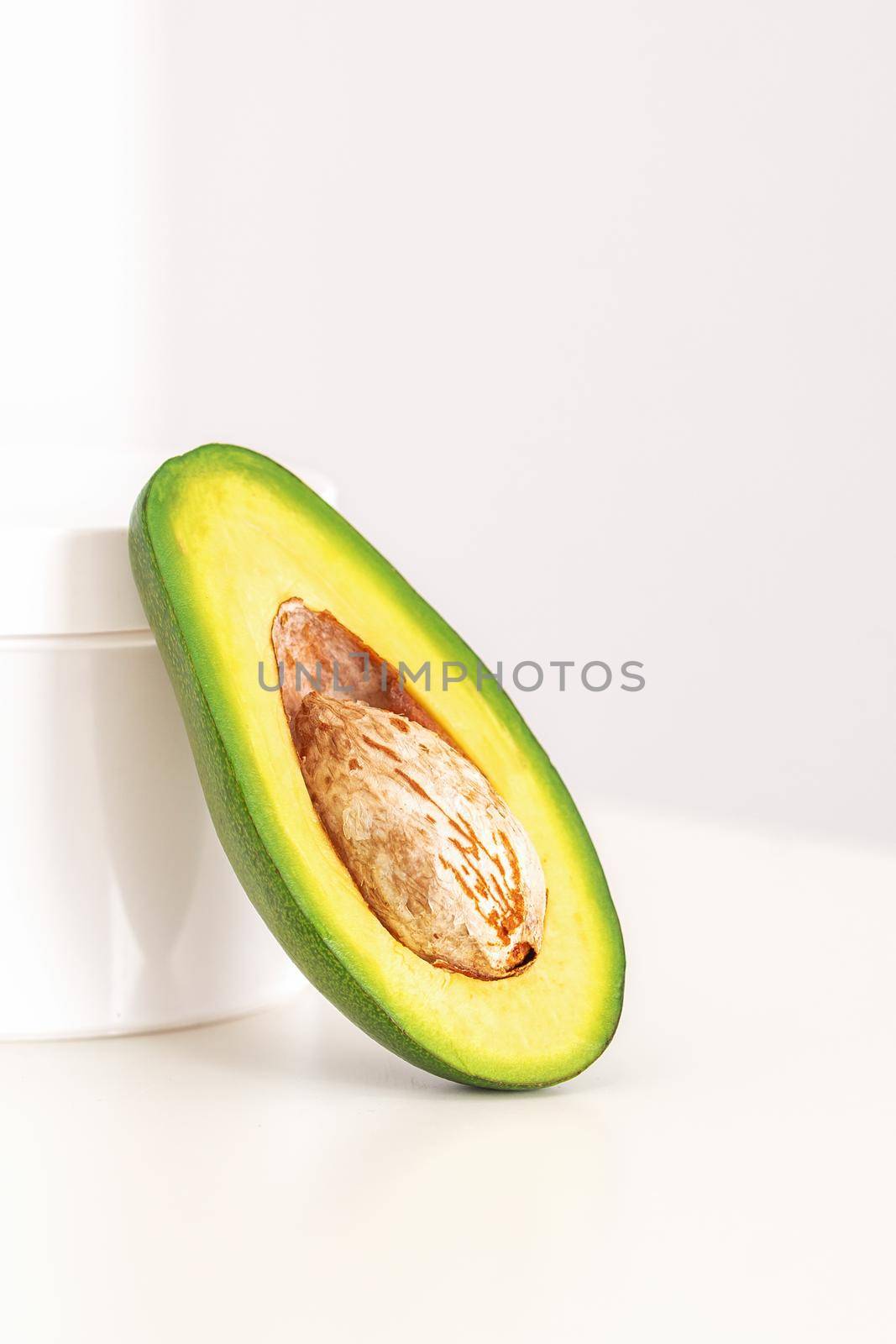 Skincare with natural cosmetics. White cosmetic jar of cream with half of the avocado near against white background, copy space, mockup