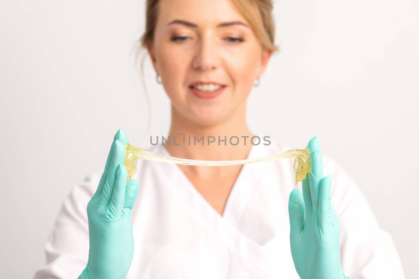 Young caucasian smiling female beautician holding wax for depilation over white background. Yellow sugar paste in hands master of depilation. Epilation concept