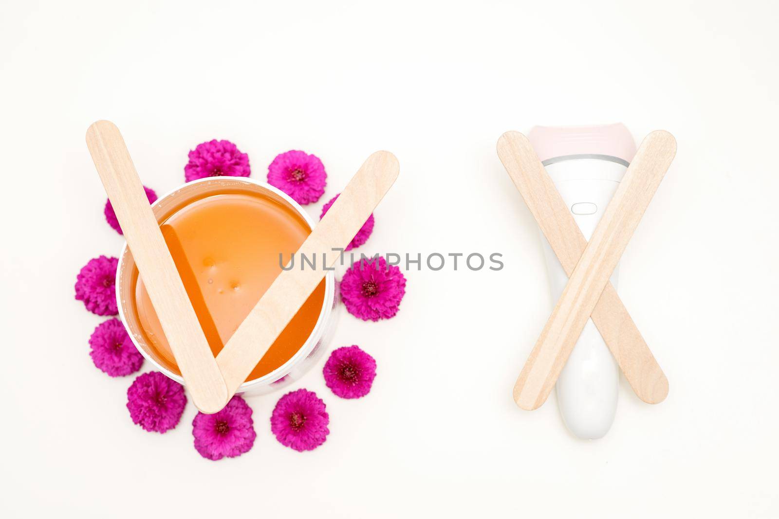 Waxing, depilation concept. Flat lay of the white cosmetic jar with sugar paste and epilator with wooden sticks lying on white background