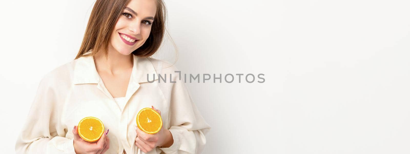 Young Caucasian smiling woman holding slices orange over isolated white background, breast health concept