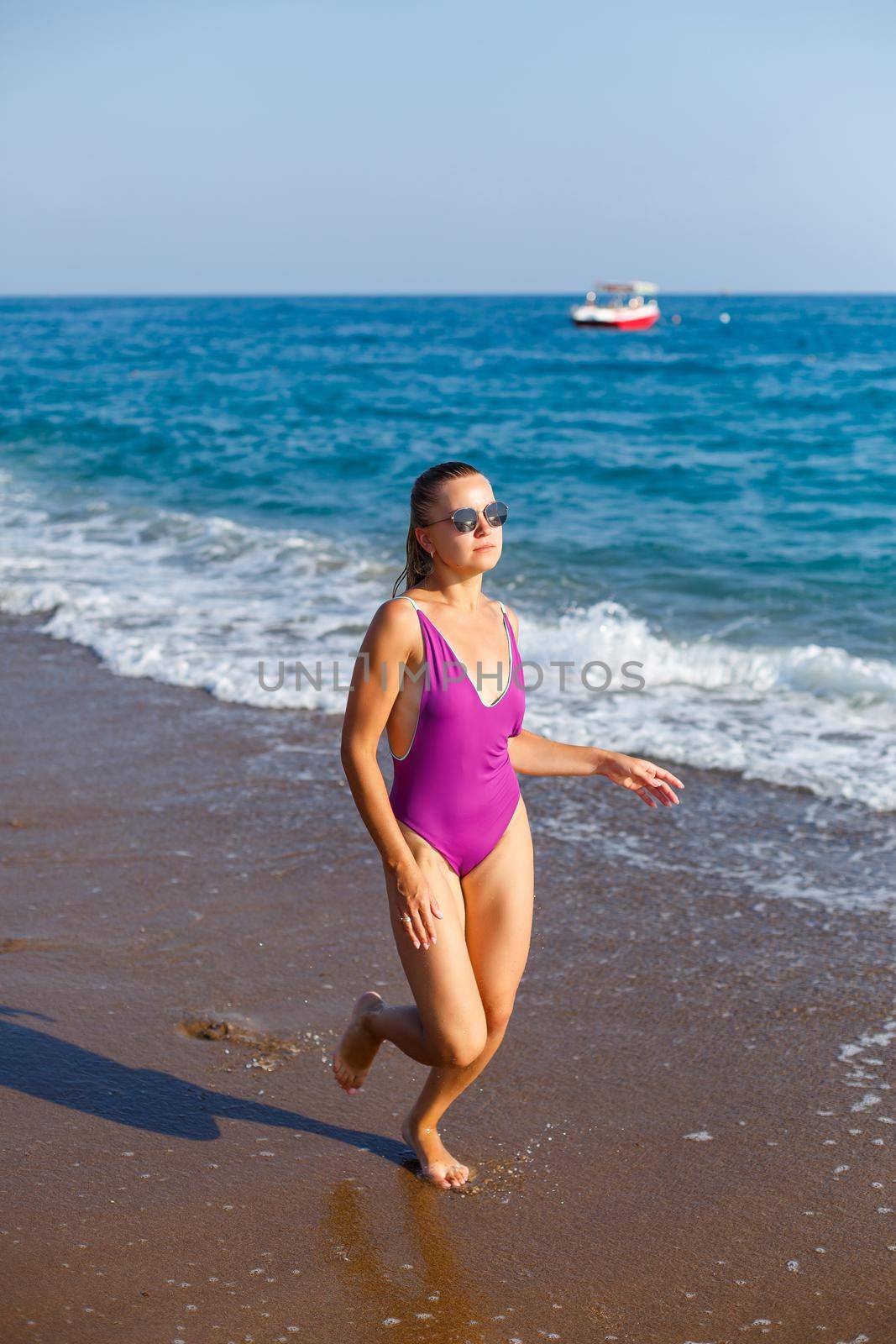 A slender woman in a swimsuit walks along the waves of the ocean on a tropical beach on a sunny day. Summer vacation concept by the sea. Selective focus