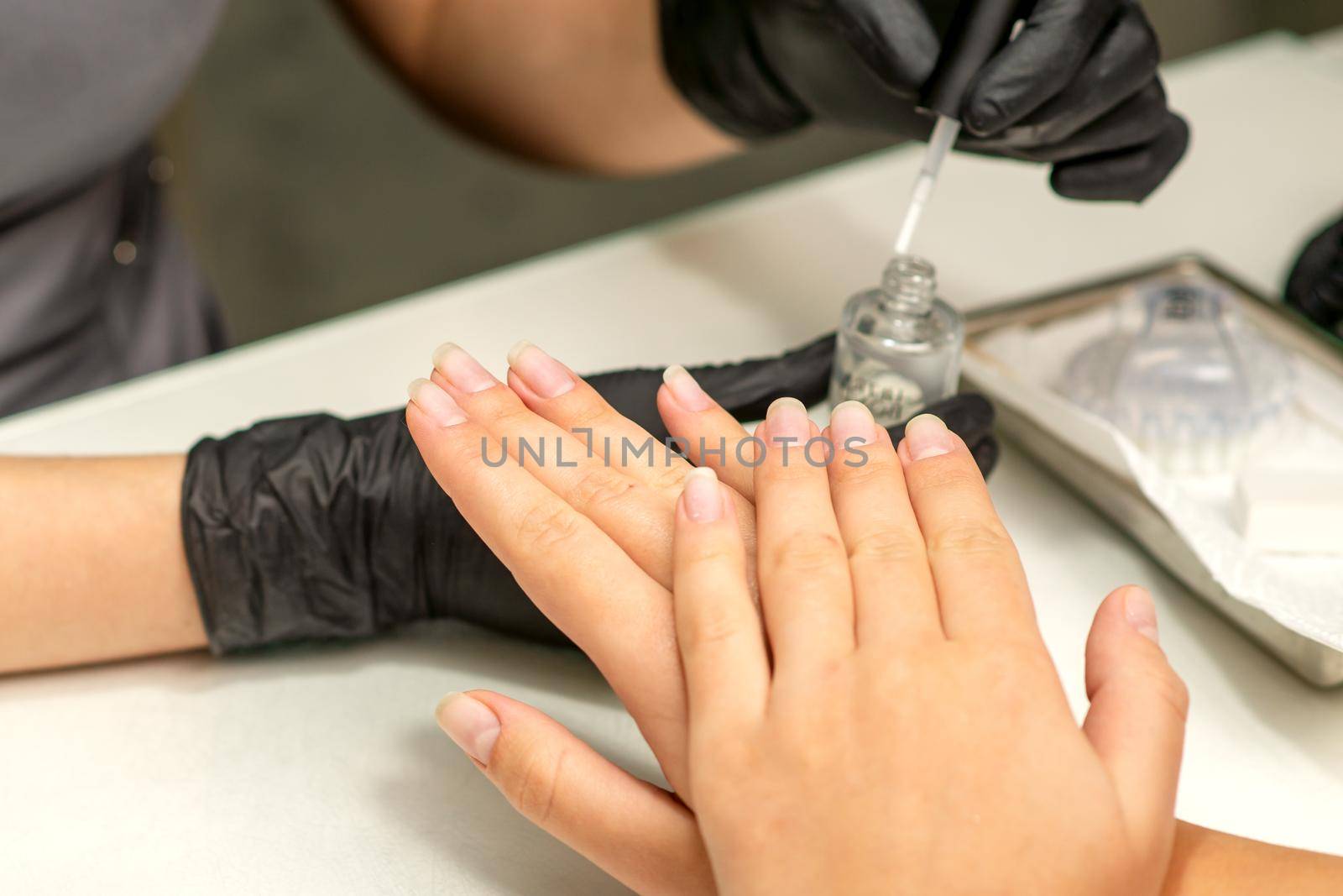 Manicure painting process. Manicure master paint the nails with transparent varnish in a nail salon, close up