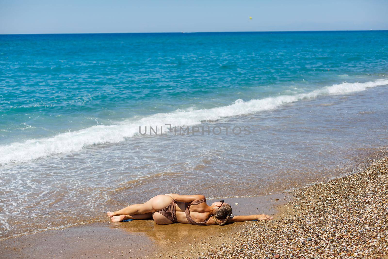 An attractive young woman in a bikini lies on the sand by the sea, relaxing on a deserted beach. Beautiful model in a swimsuit resting on the fine sand on a tropical island