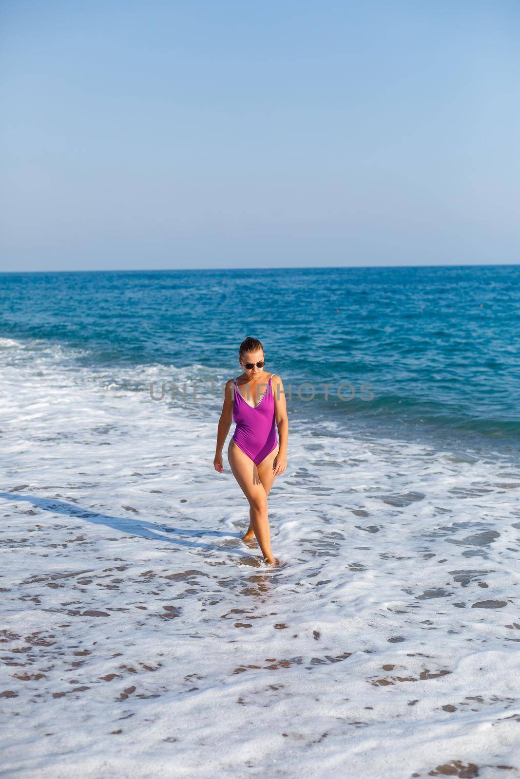 A young beautiful woman with a toned body in a bright swimsuit walks along the sandy beach. Summer vacation at the sea. Mediterranean Turkish Sea. Selective focus