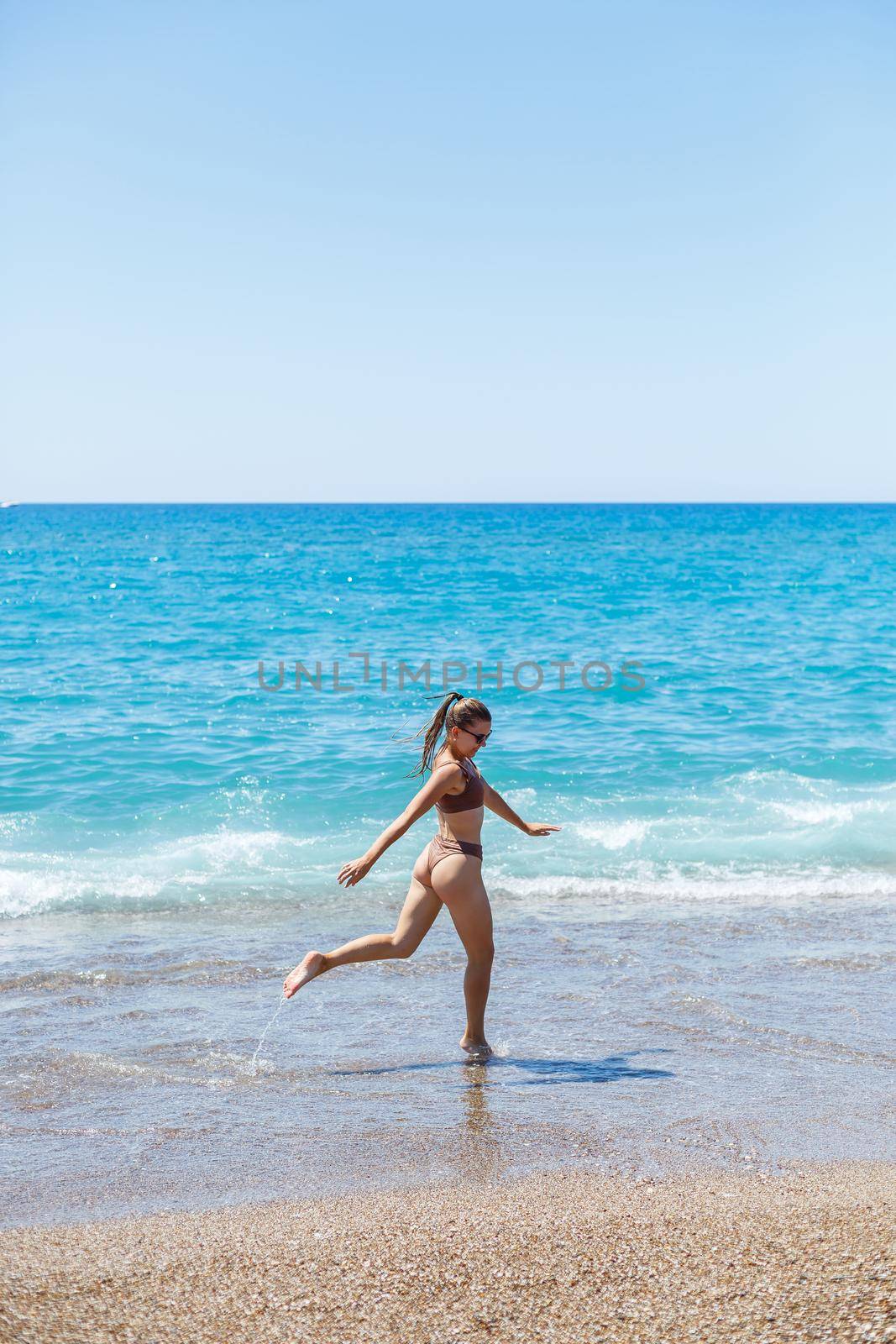 A slender beautiful young woman in a swimsuit walks along the beach by the sea. Summer vacation concept. Selective focus