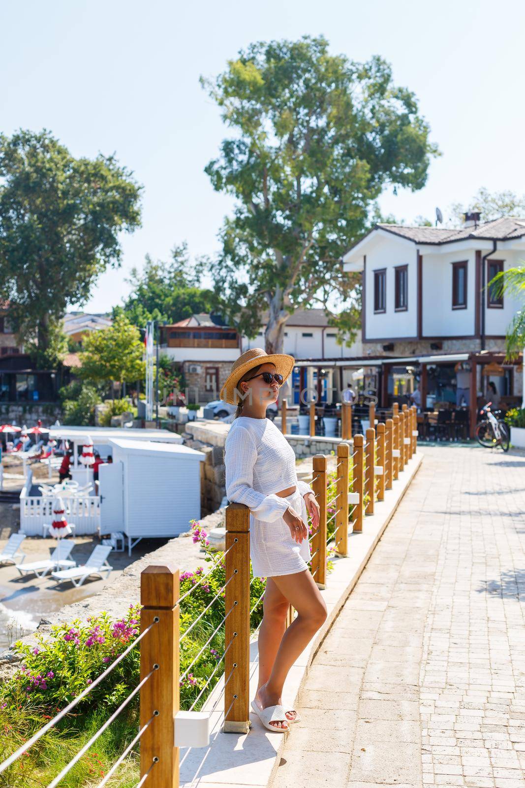A young slender tanned woman in white shorts and a T-shirt, wearing sunglasses and a hat. Walk on a hot sunny day in the ancient city