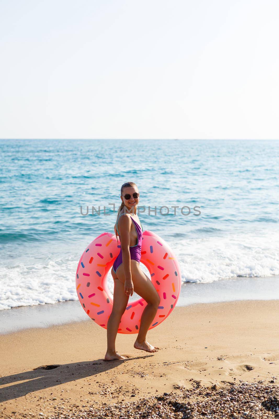 Woman on the beach walks with an inflatable ring in the sea, walks relaxing in a tropical paradise for relaxation. Young model sunbathing on summer vacation.