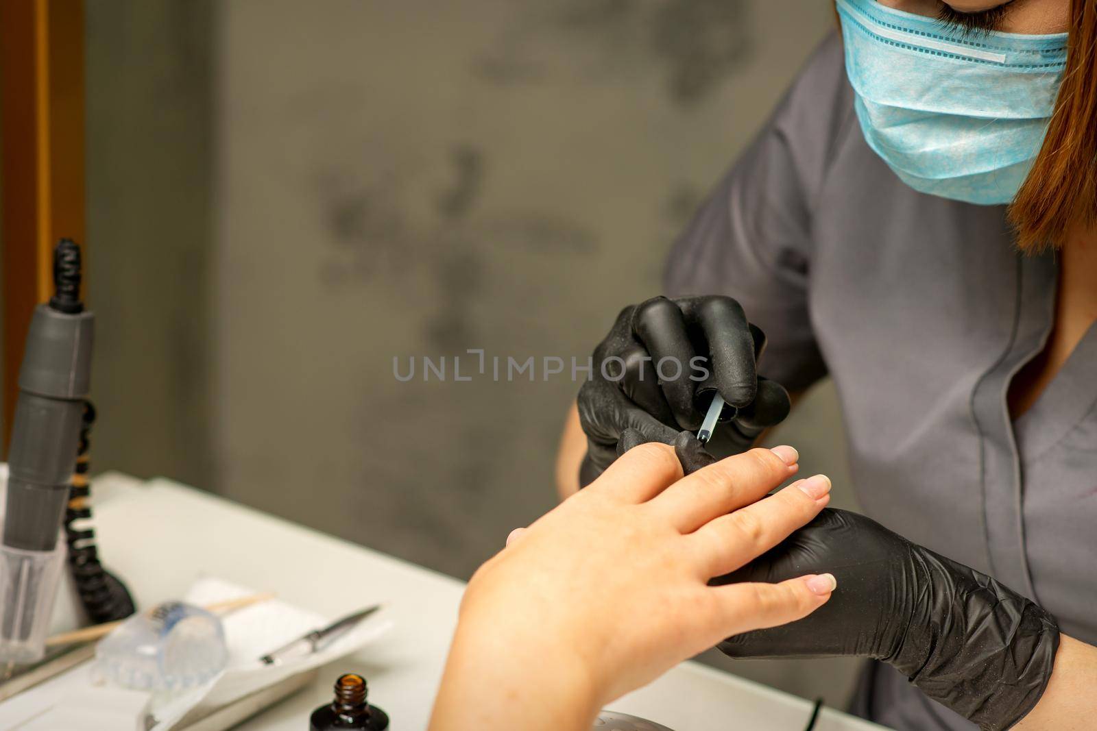 Manicure painting process. Manicure master paint the nails with transparent varnish in a nail salon, close up