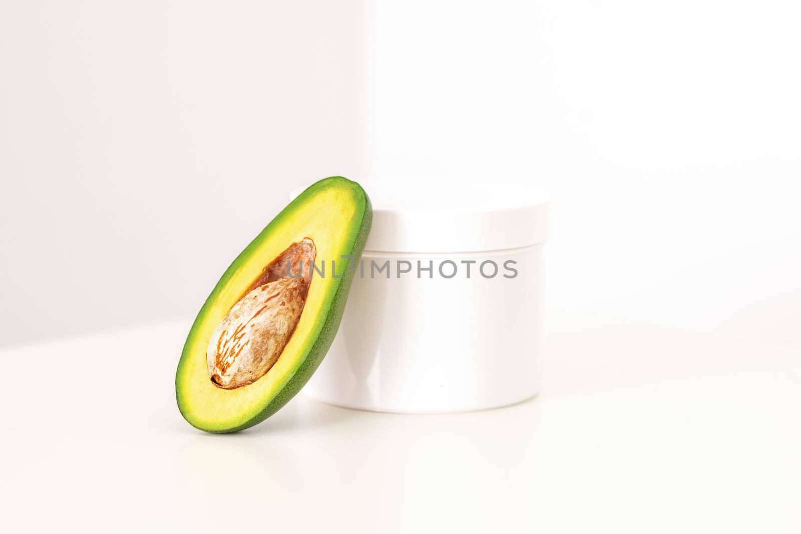 Skincare with natural cosmetics. White cosmetic jar of cream with half of the avocado near against white background, copy space, mockup. by okskukuruza