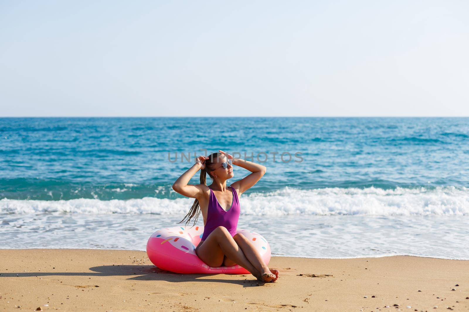 Attractive young woman in a bright swimsuit posing on the beach with an inflatable ring. Beautiful blond woman with long hair relaxing by the ocean. The concept of a sports model, swimwear