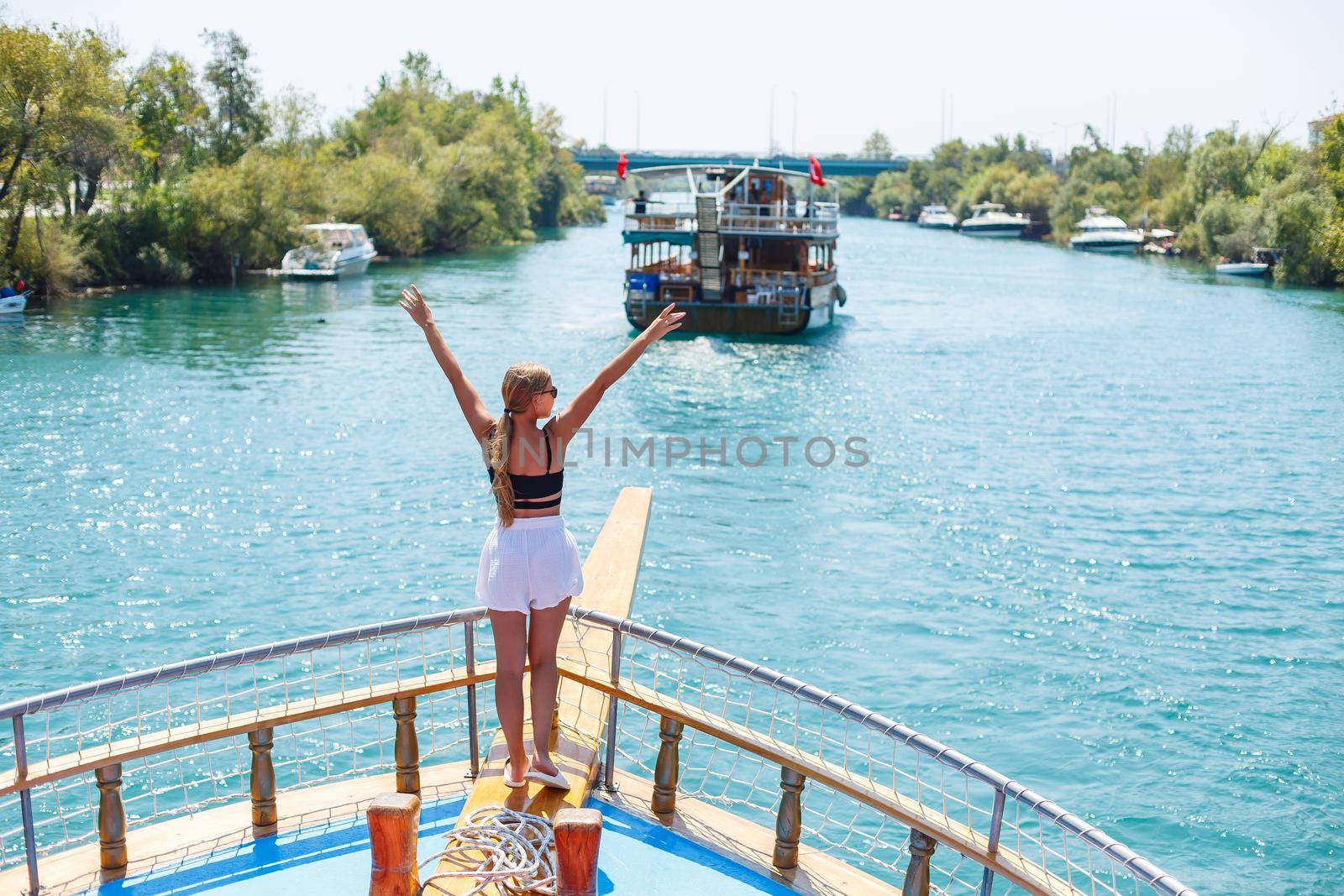 A young slender tanned woman in white shorts and a top, wearing sunglasses. Walk on a hot sunny day on a yacht along the river