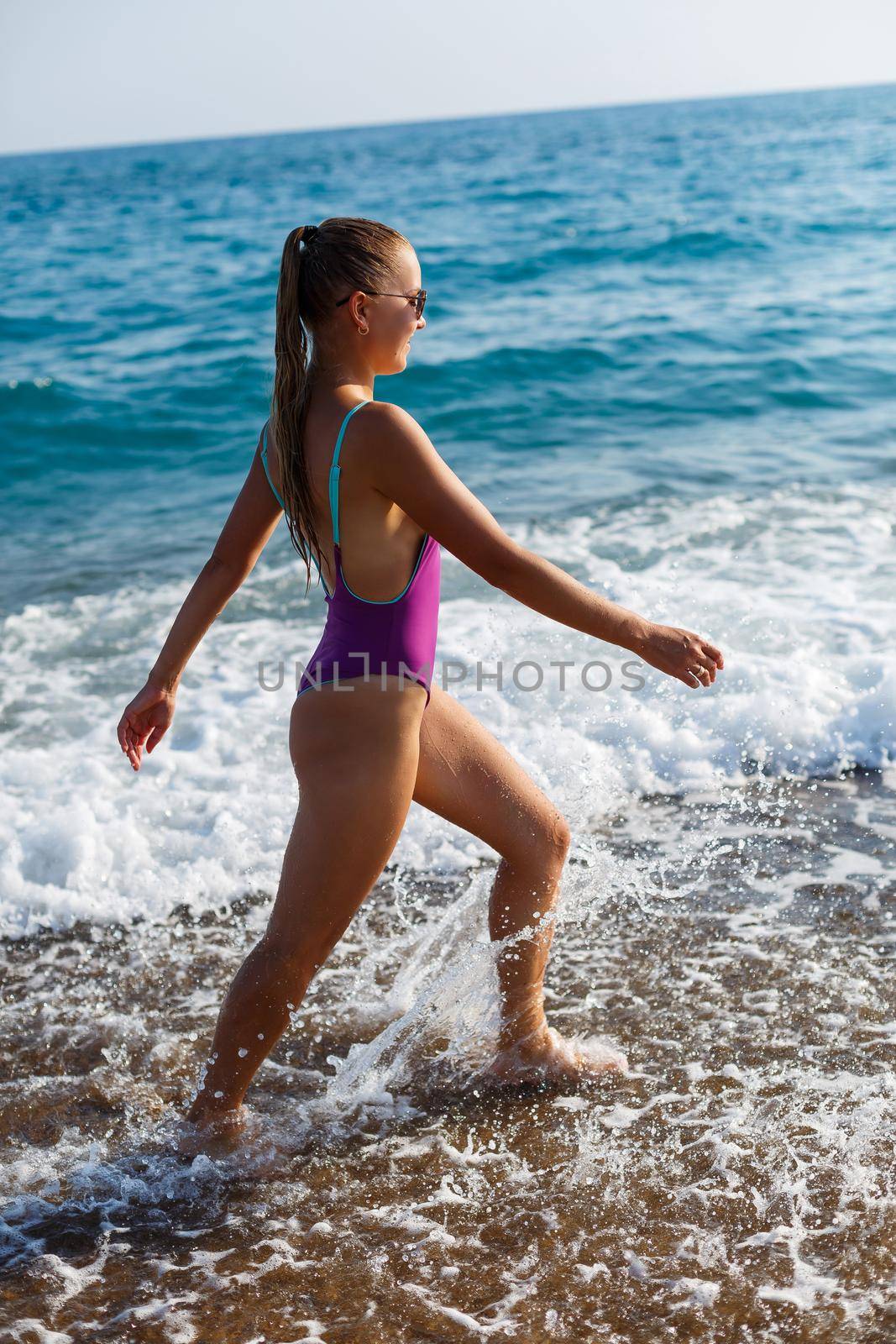 A young beautiful woman with a toned body in a bright swimsuit walks along the sandy beach. Summer vacation at the sea. Mediterranean Turkish Sea. Selective focus