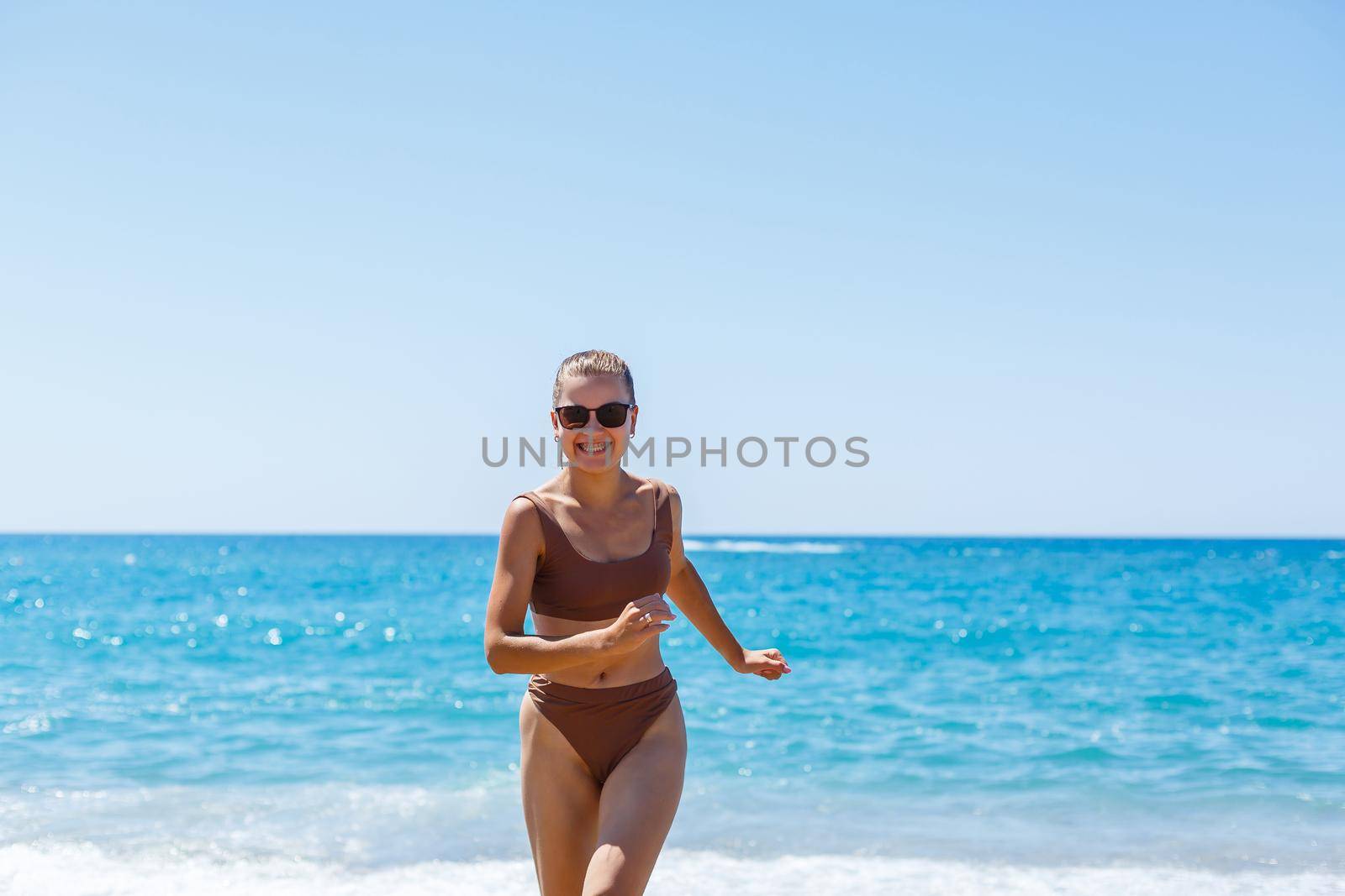 A slender beautiful young woman in a swimsuit walks along the beach by the sea. Summer vacation concept. Selective focus