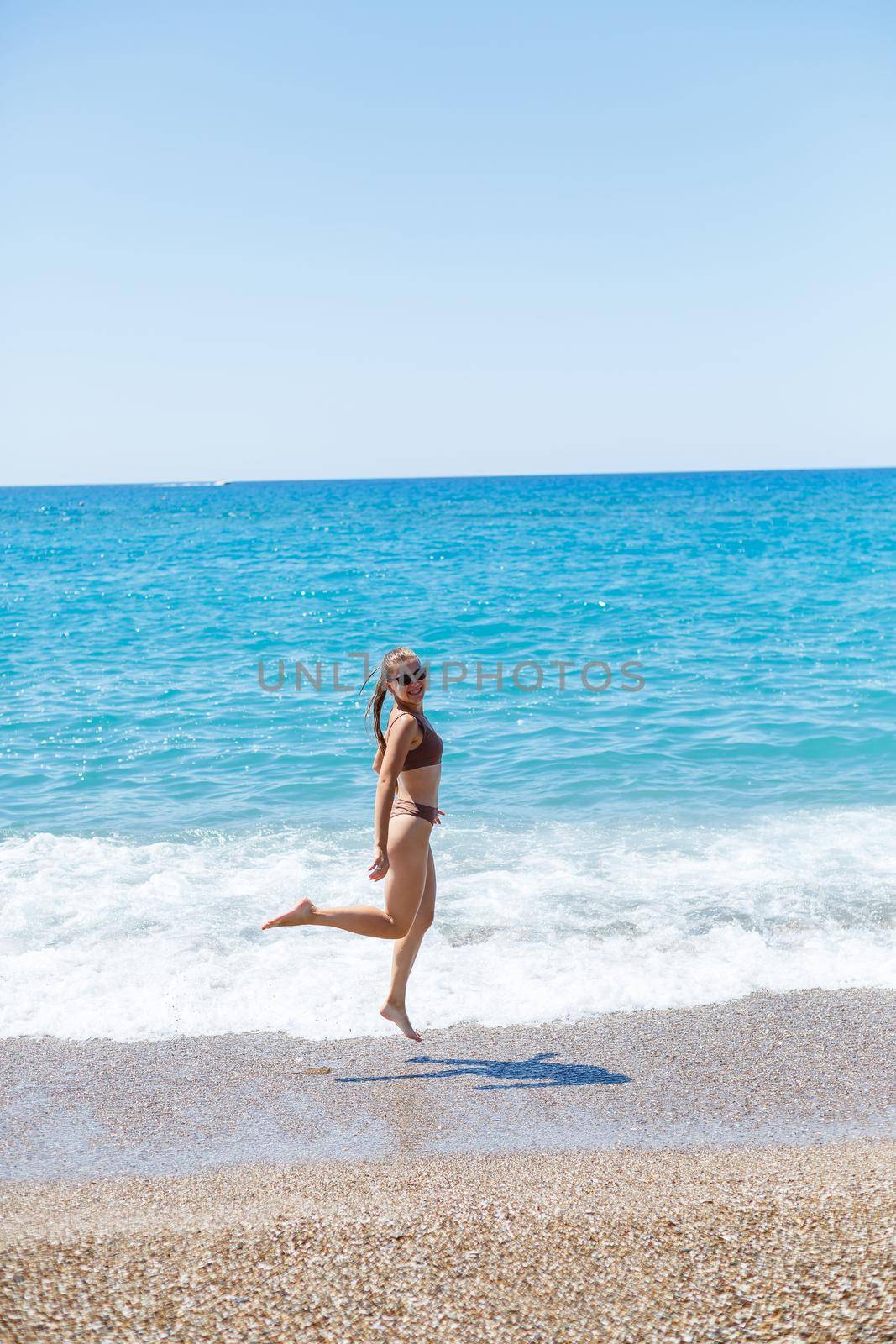 A slender beautiful young woman in a swimsuit walks along the beach by the sea. Summer vacation concept. Selective focus