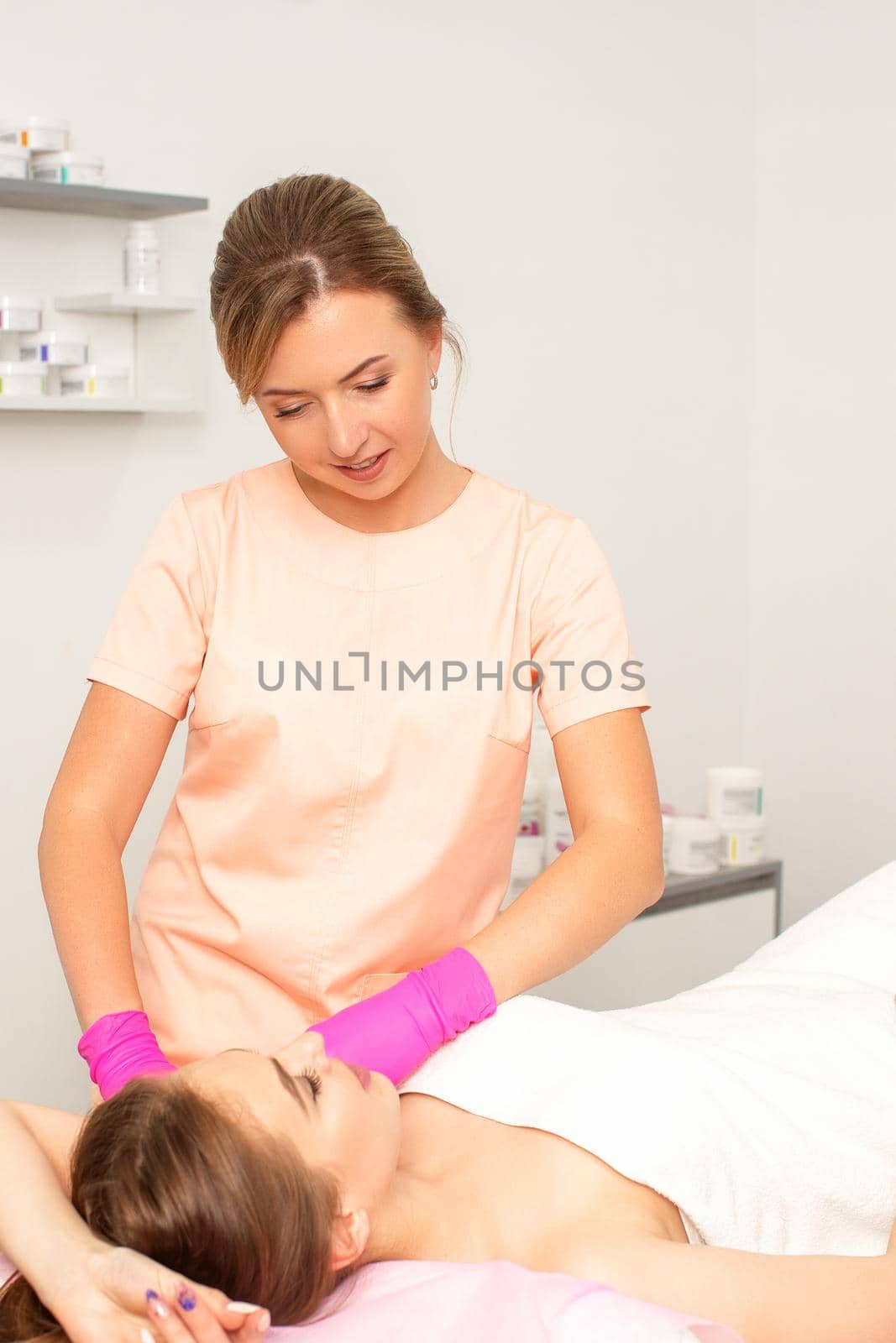 Beautician with a patient during sugaring. The cosmetologist waxes the female armpit