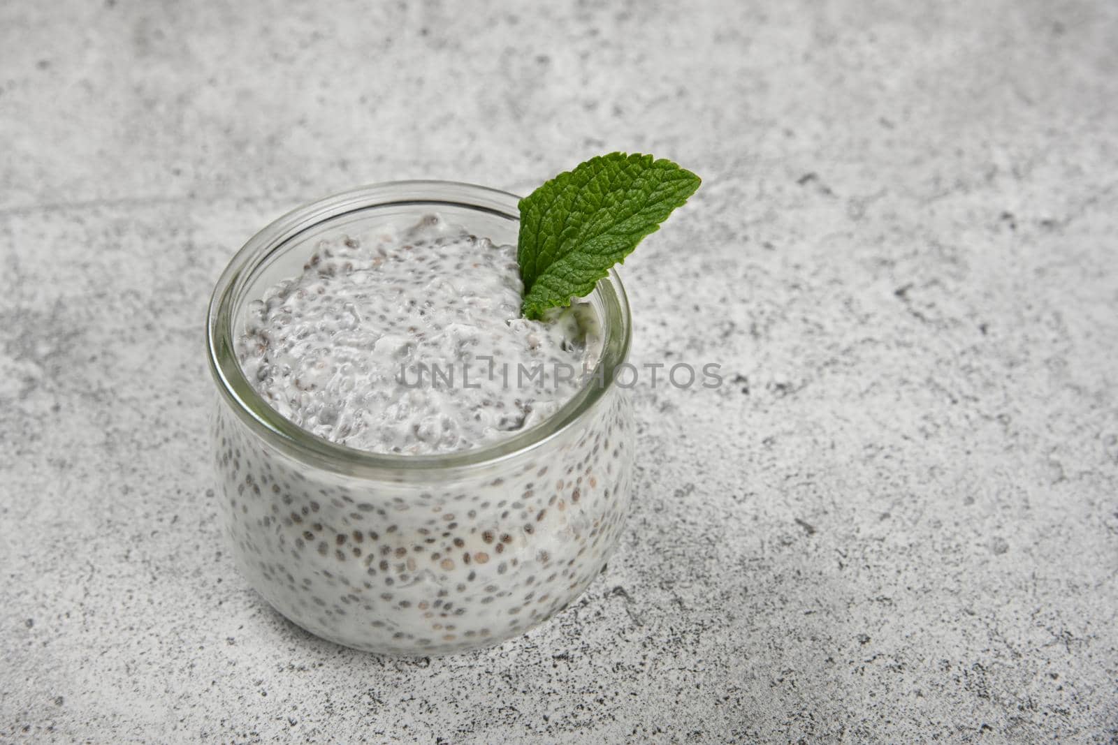 Close up one transparent glass jar of chia seeds pudding dessert with coconut milk on table, high angle view