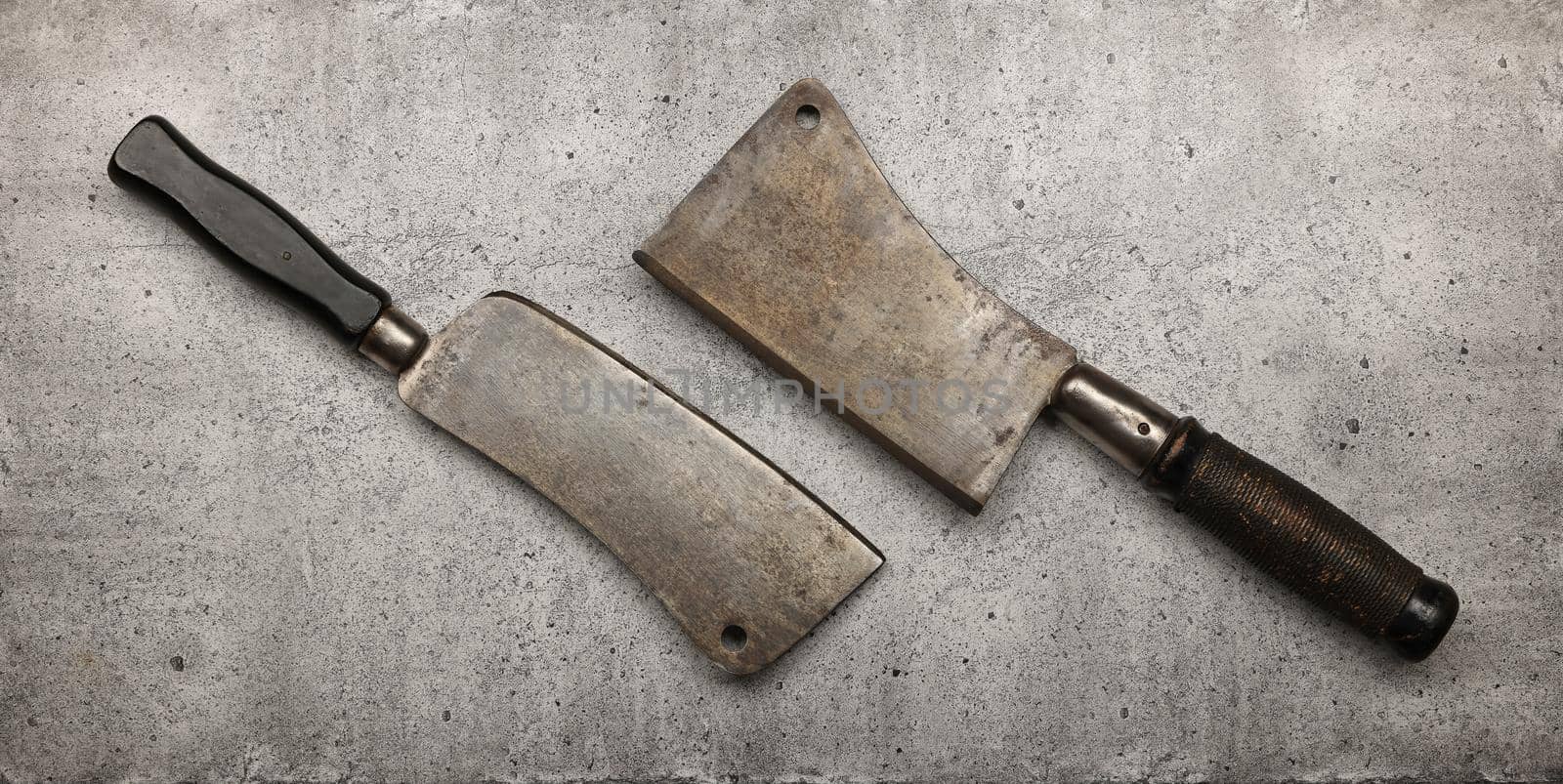 Close up two vintage butcher meat cleavers on cutting board or grunge gray stone table surface with copy space, elevated top view, directly above