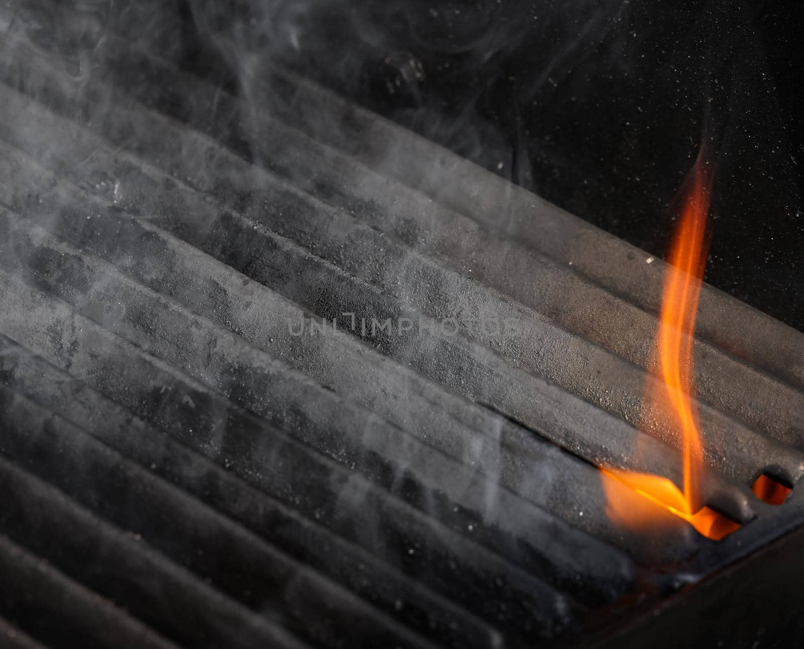 Close up empty cast iron metal BBQ grill grate with fire flames and smoke, hot charcoal below, high angle view