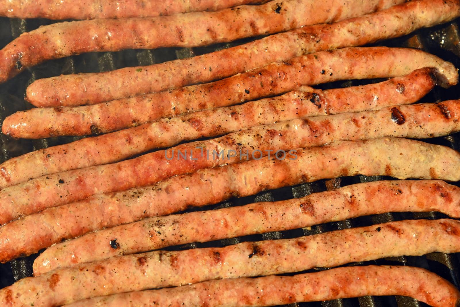 Close up cooking meat sausages on grill, smoking and broiling them, high angle view