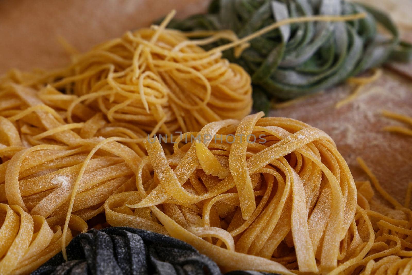 Close up cooking fresh handmade traditional Italian tagliatelle pasta, uncooked black, green and classical past on wooden table, high angle view