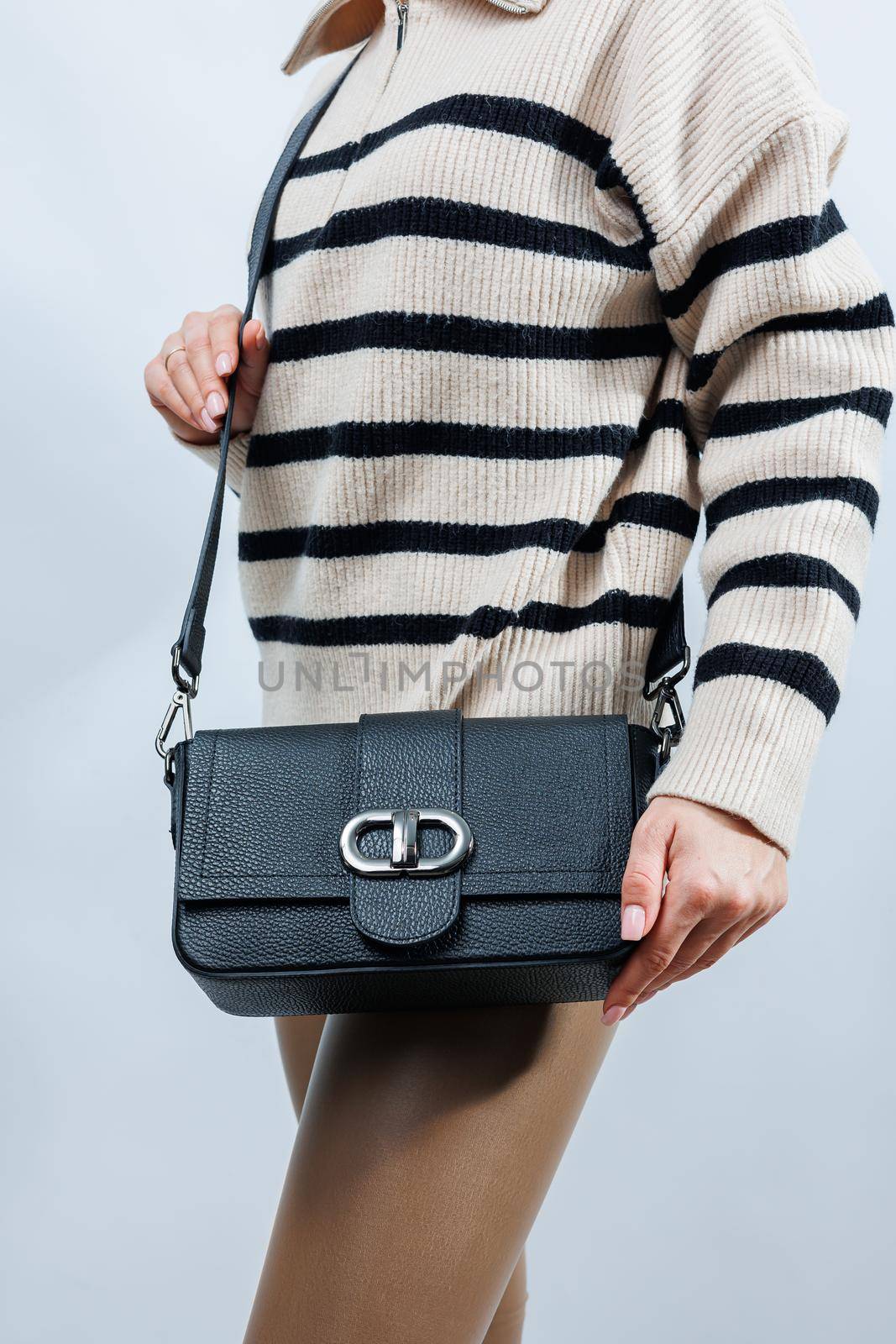 Beautiful young woman posing on a white background with a black handbag over her shoulder. A woman is holding a black leather shoulder bag. Women's fashion concept.