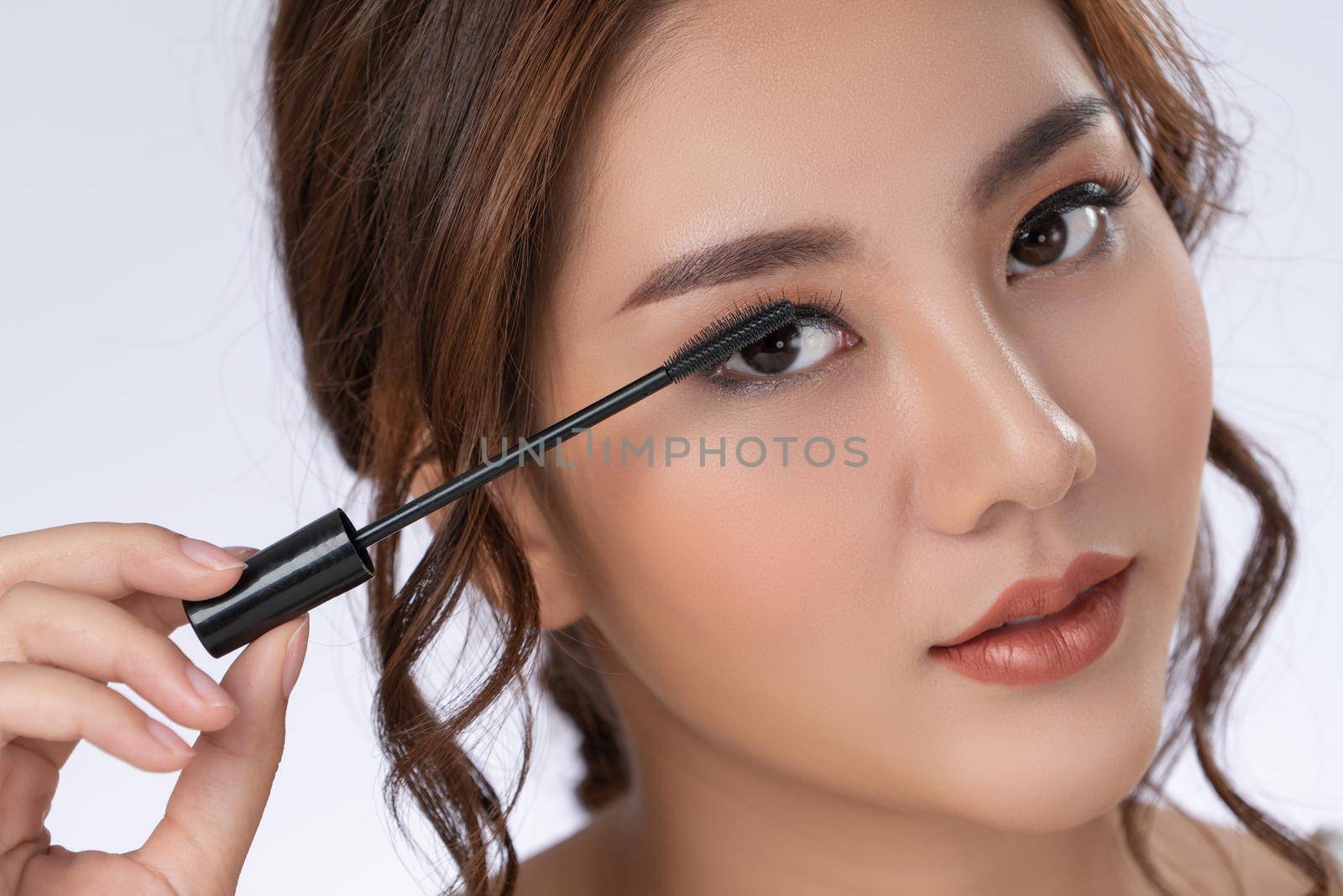 Closeup gorgeous young woman putting black mascara on her long eyelashes with brush. Beauty cosmetic concept. Female model with perfect skin.