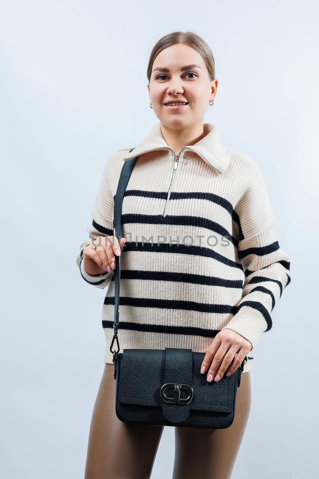 Beautiful young woman posing on a white background with a black handbag over her shoulder. A woman is holding a black leather shoulder bag. Women's fashion concept.