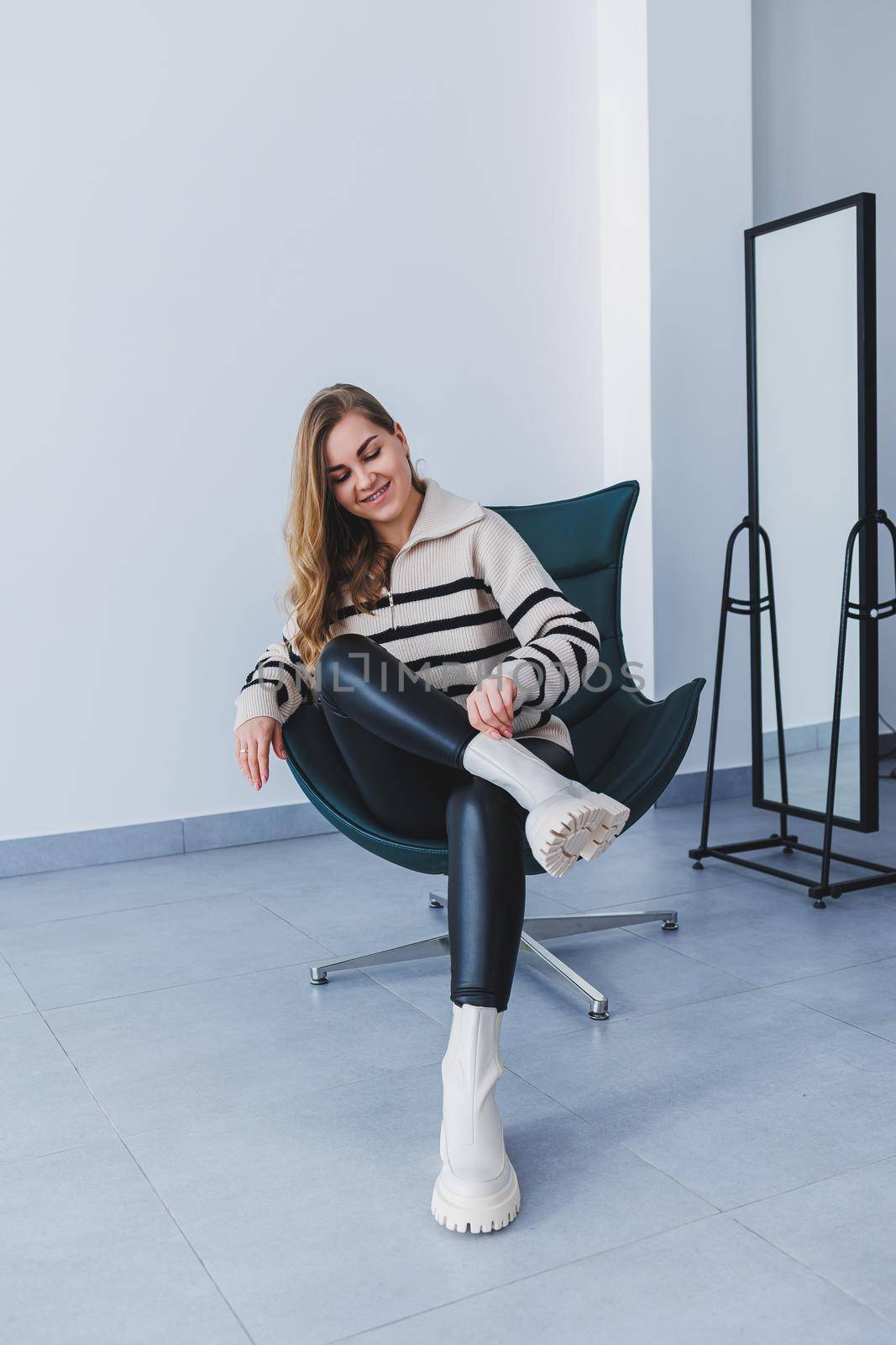 A young beautiful woman is sitting in a chair, wearing white leather boots from a new collection of shoes for spring.