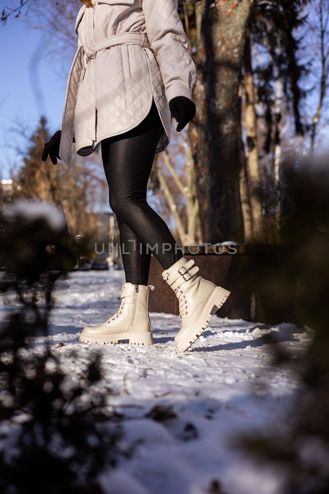 Woman in fashionable white boots on white snow, close-up. Women's legs in stylish winter leather boots