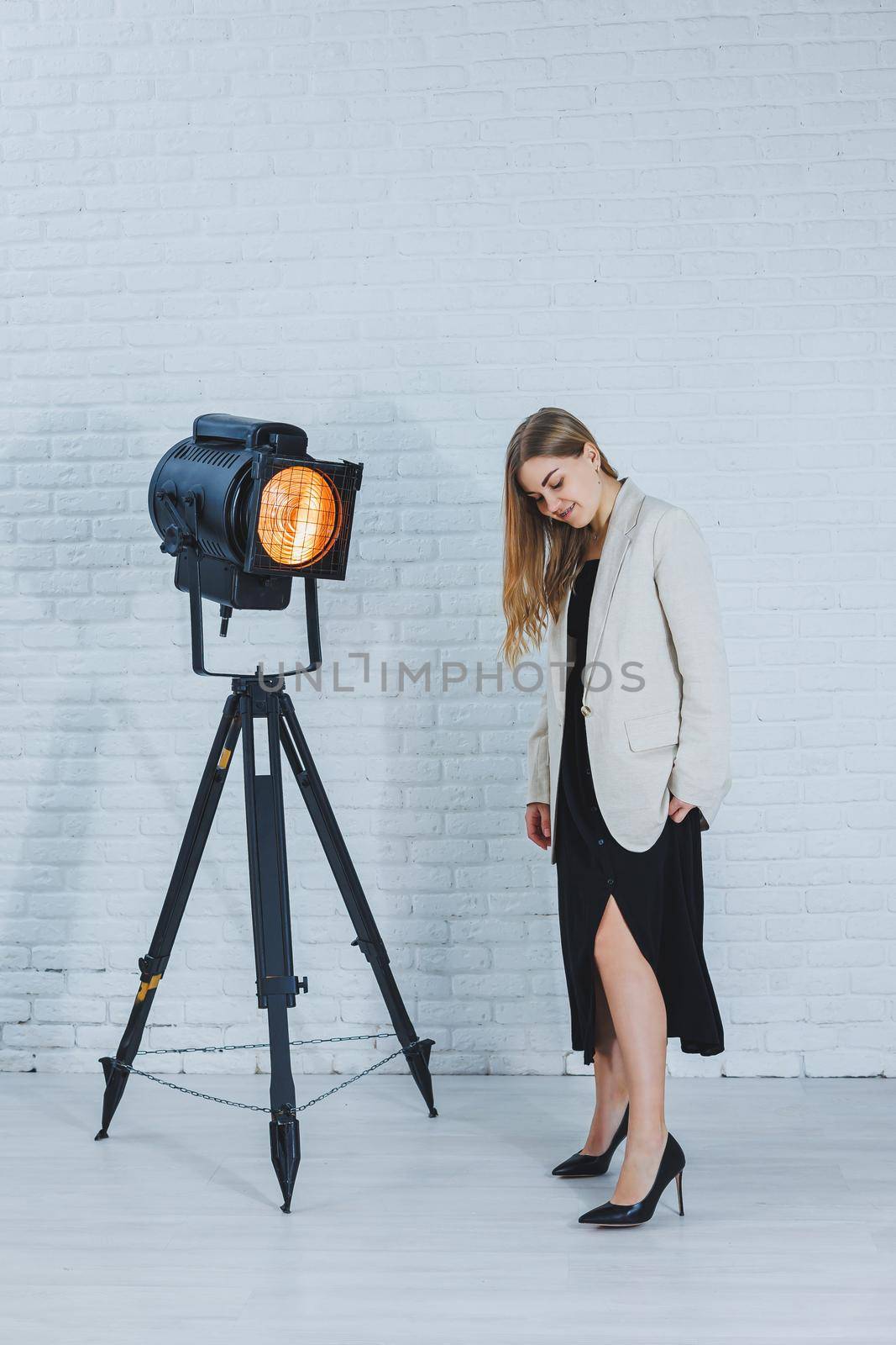 Gorgeous slender brown-haired woman in a black dress and a beige jacket, long bare legs and high heels. Black pumps on female feet