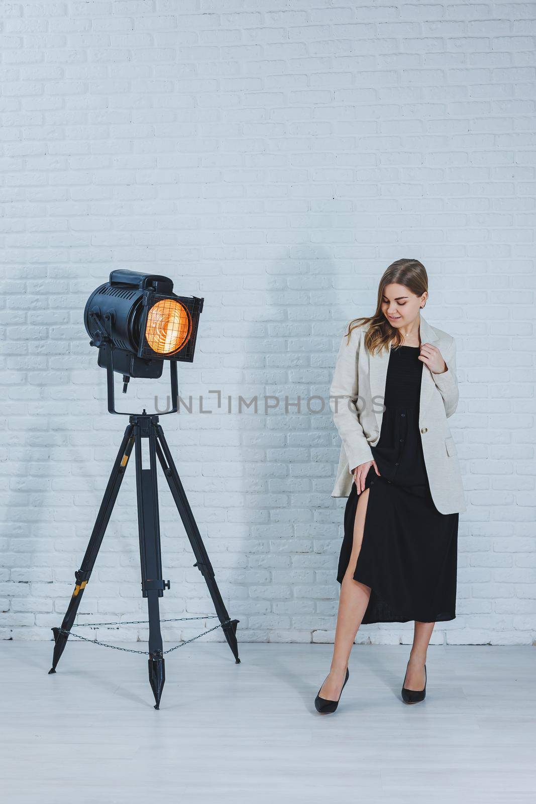 Gorgeous slender brown-haired woman in a black dress and a beige jacket, long bare legs and high heels. Black pumps on female feet by Dmitrytph