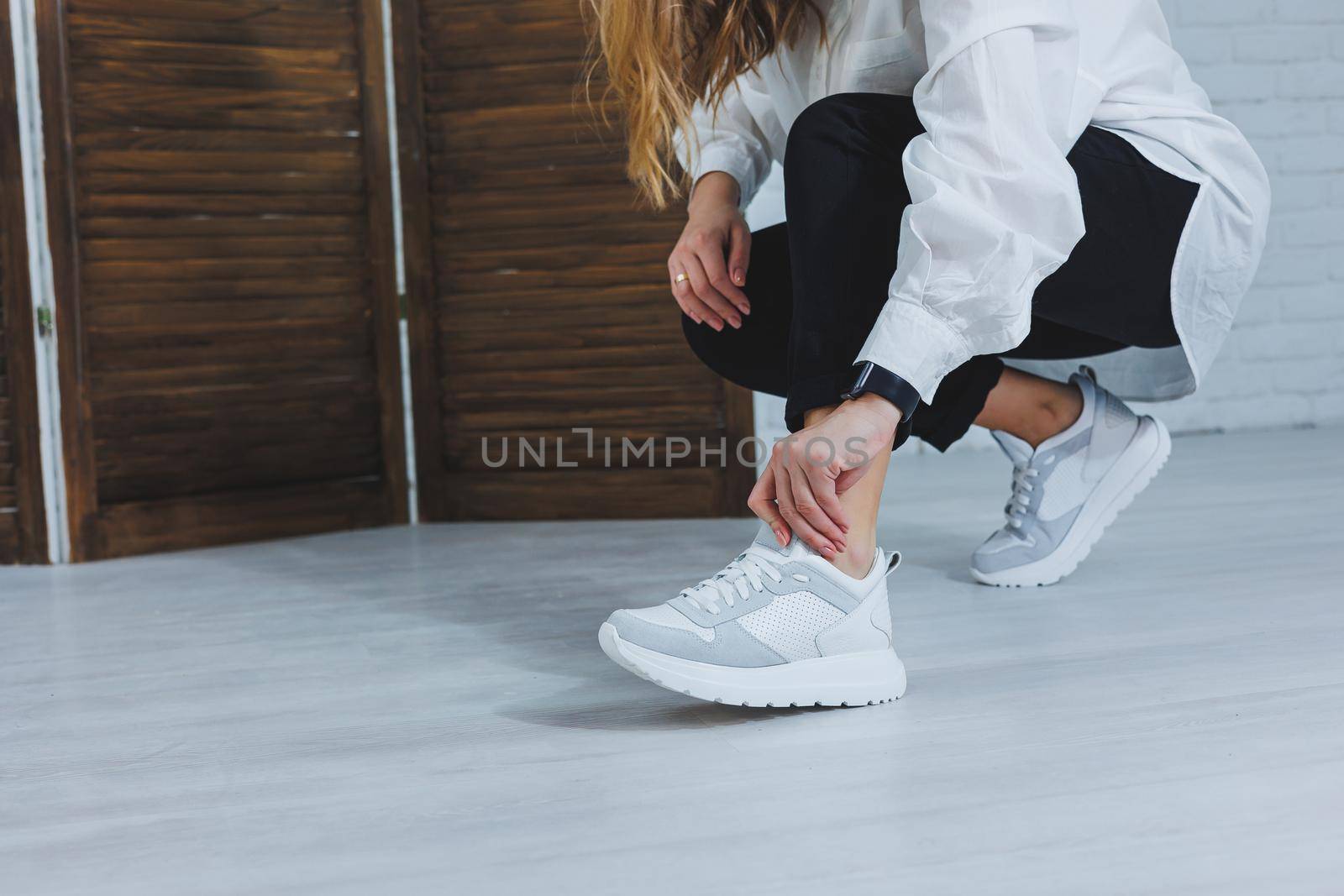 Beautiful women's shoes with legs, leather white sneakers, in the interior of a room or office, shoes for a woman, black trousers and white sneakers, casual and modern style, modern and trendy
