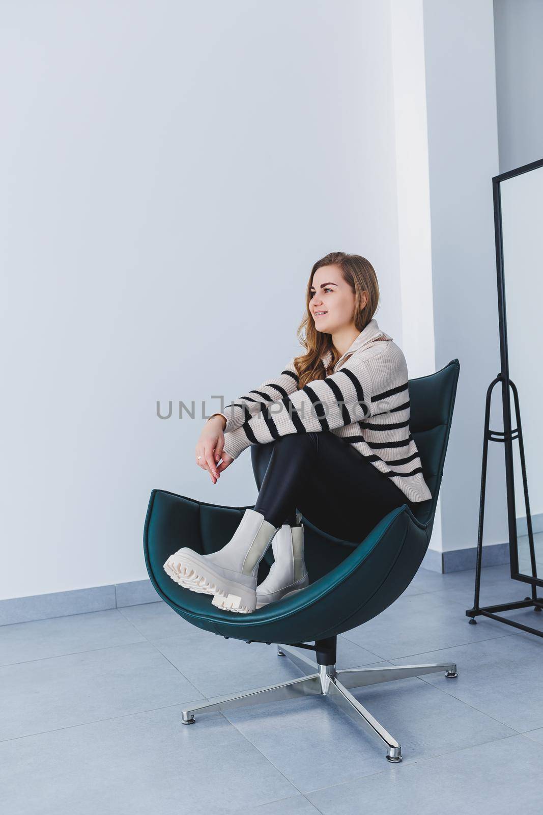 A young beautiful woman is sitting in a chair, wearing white leather boots from a new collection of shoes for spring.