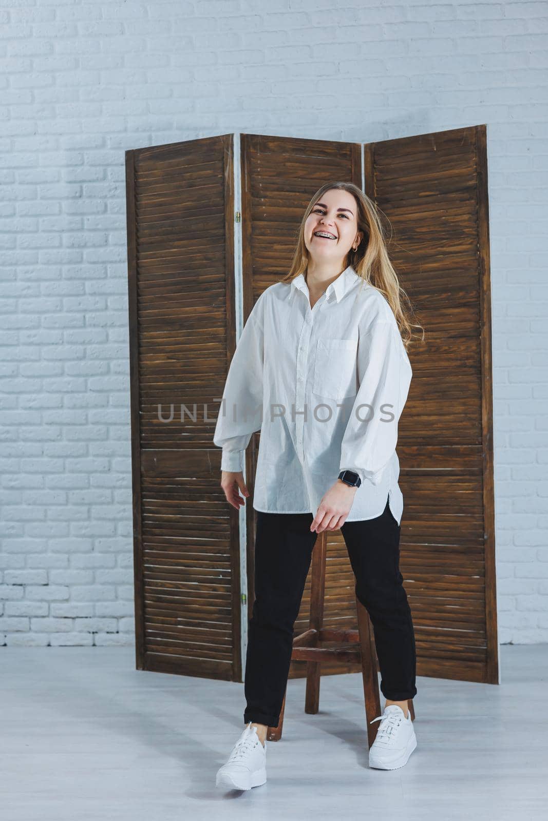 A beautiful stylish woman is wearing a white cotton shirt and black pants. Cheerful emotional girl in white sneakers