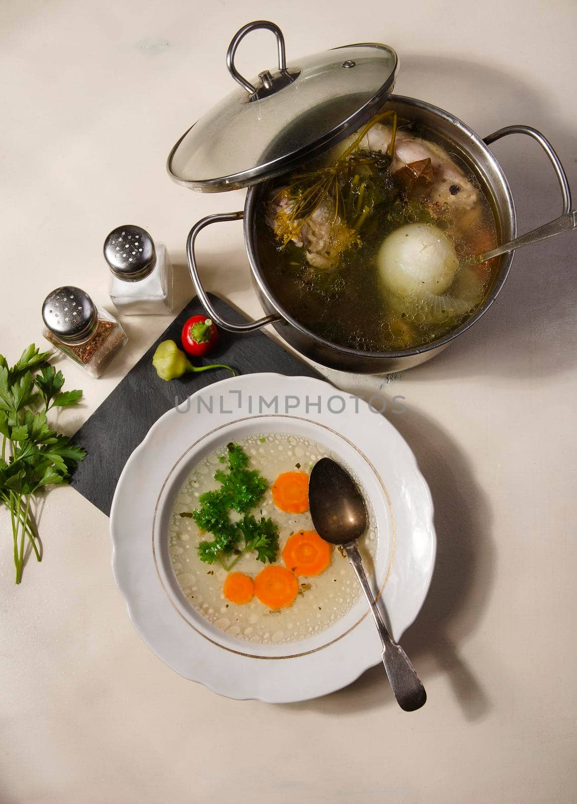 A plate and a pot with fresh home made chiken broth with carrot and spices on white table, flat lay, top view.