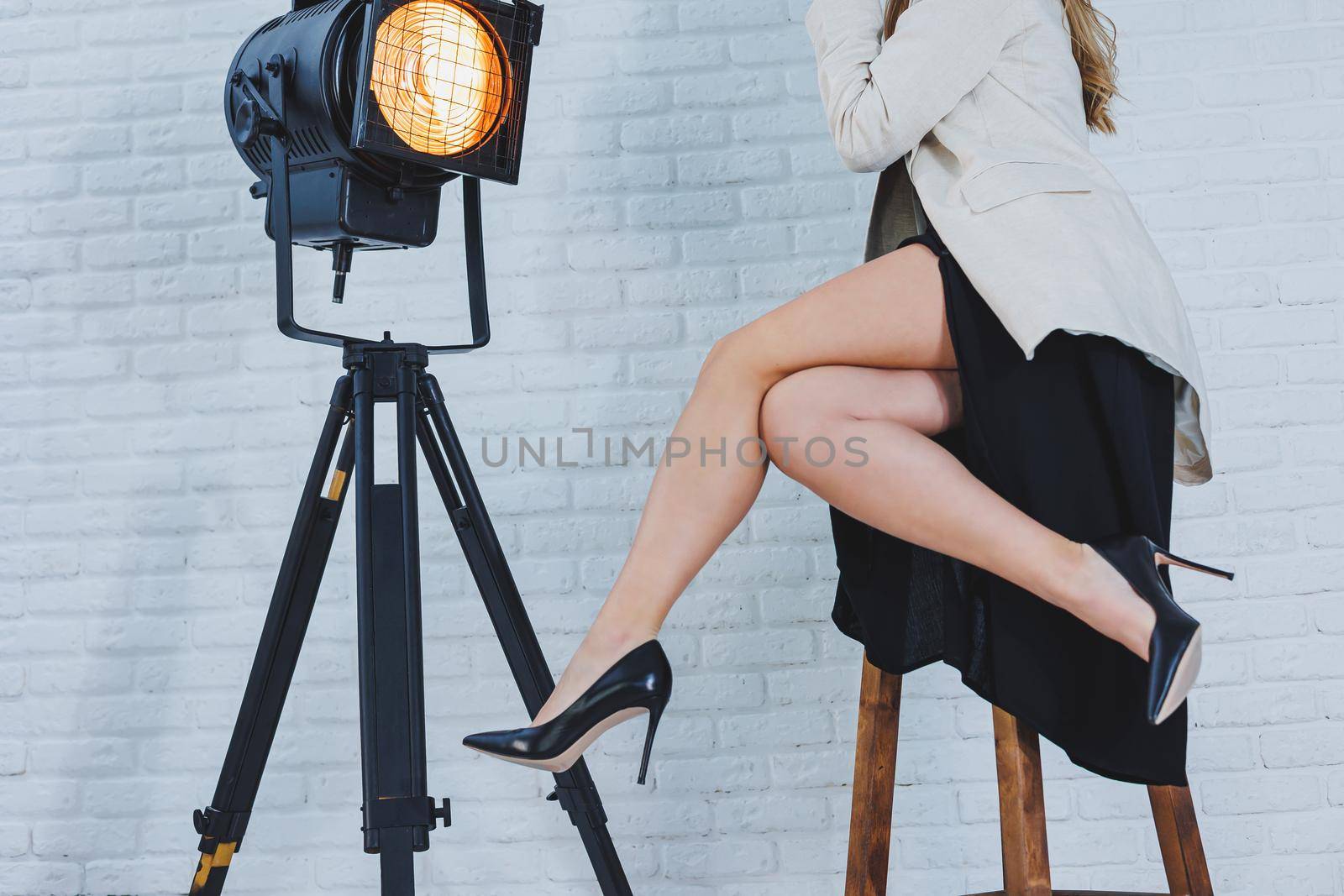 Close-up portrait of female legs in high heels. A lady in a black dress sits with long slender legs in black high-heeled shoes. Classic women's shoes