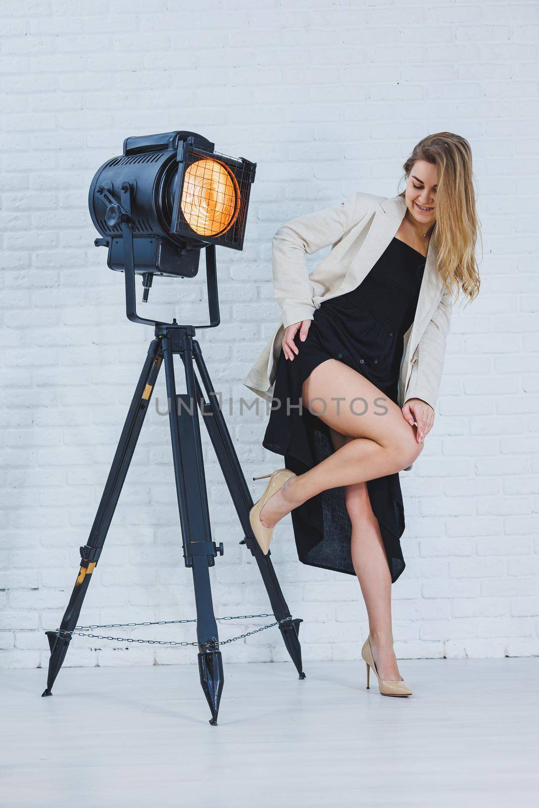 Beautiful young female legs in beige high-heeled shoes, a black long dress and a beige jacket. Open autumn and spring outfit with heeled shoes