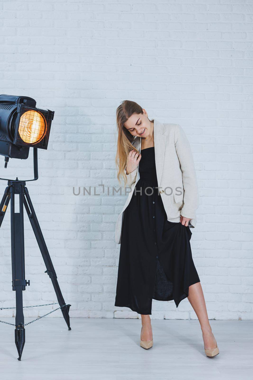 Beautiful young female legs in beige high-heeled shoes, a black long dress and a beige jacket. Open autumn and spring outfit with heeled shoes by Dmitrytph
