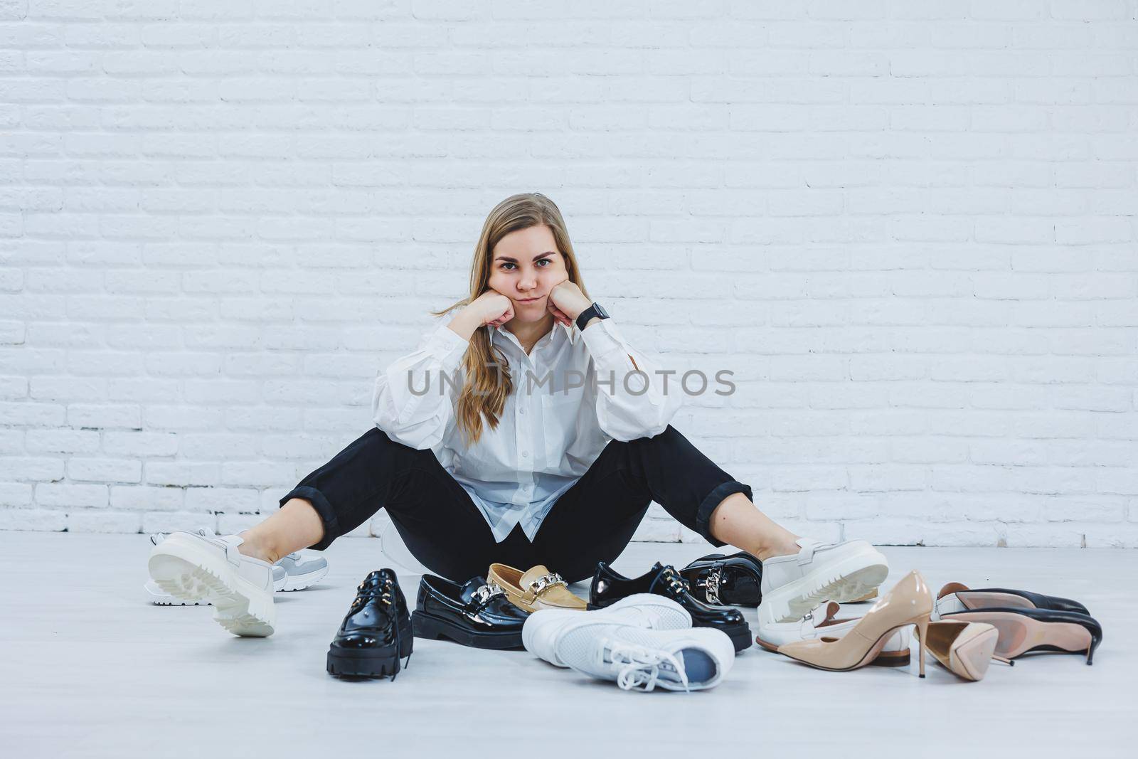 Stylish blonde choosing shoes while sitting on the floor. Side view of a lot of women's shoes on the floor, a choice of stylish shoes.
