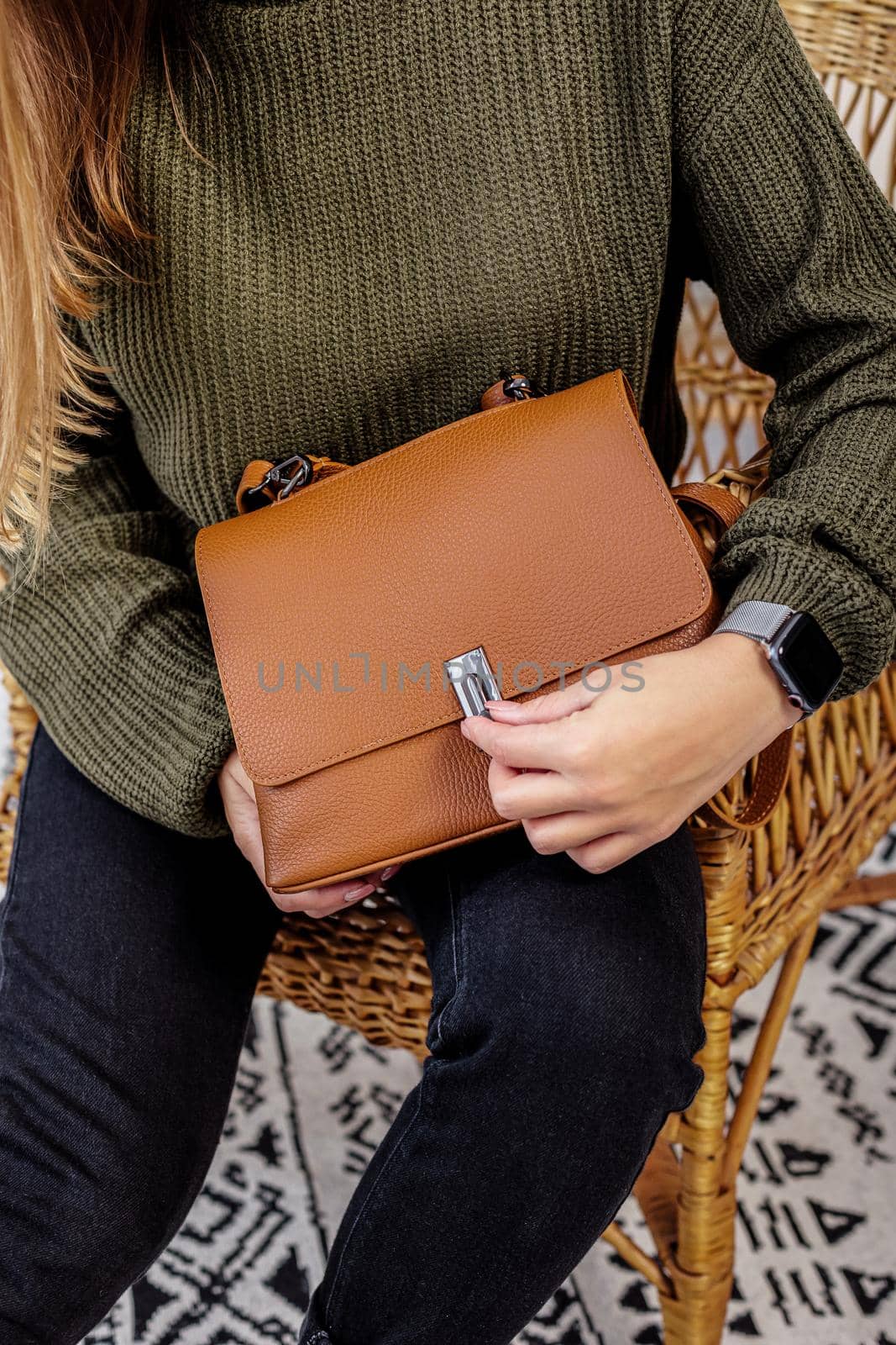 A woman holds a leather brown fashionable handbag in her hands. New collection of women's handbags