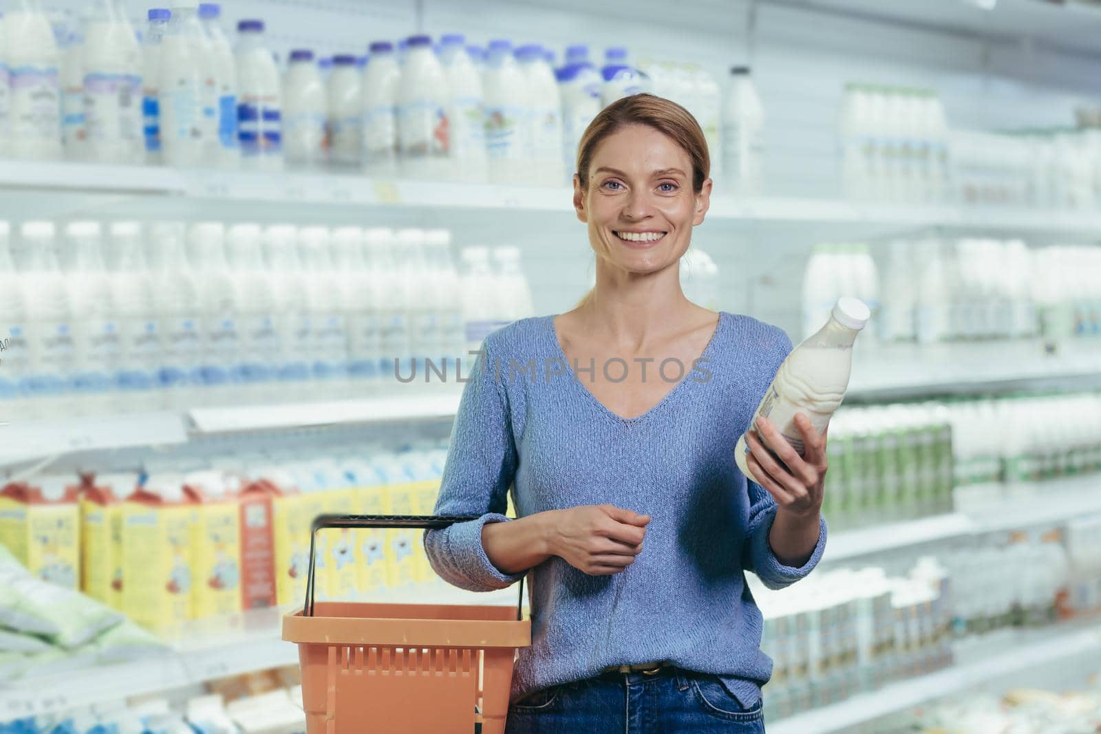 Portrait of a female buyer in a supermarket, a blonde housewife looking at the camera in the dairy department chooses milk and yogurt.