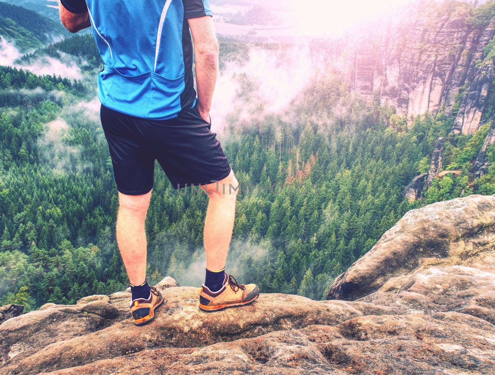 Hiker legs climbing on sunrise mountain peak rock. Slim  legs of a mountain hiker with hiking boots on exposed rock.