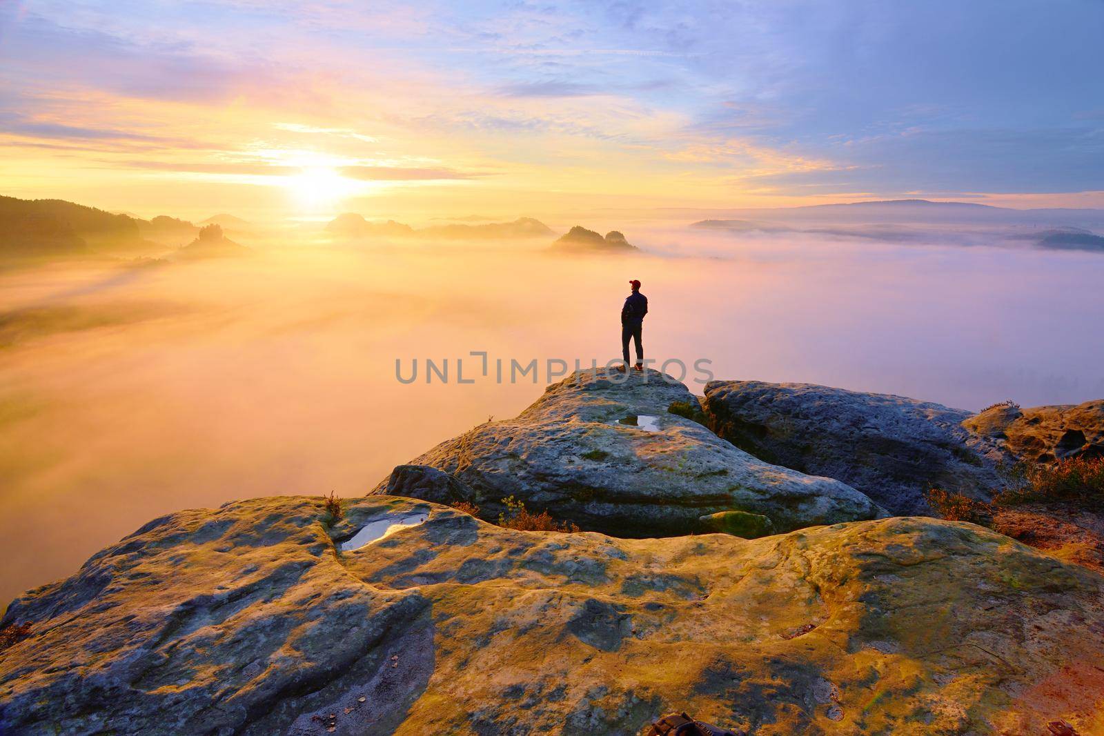 Sharp rear man silhouette on rocky peak. Satisfy hiker enjoy view. Tall man on rocky cliff watching down to landscape. Vivid and strong vignetting effect.