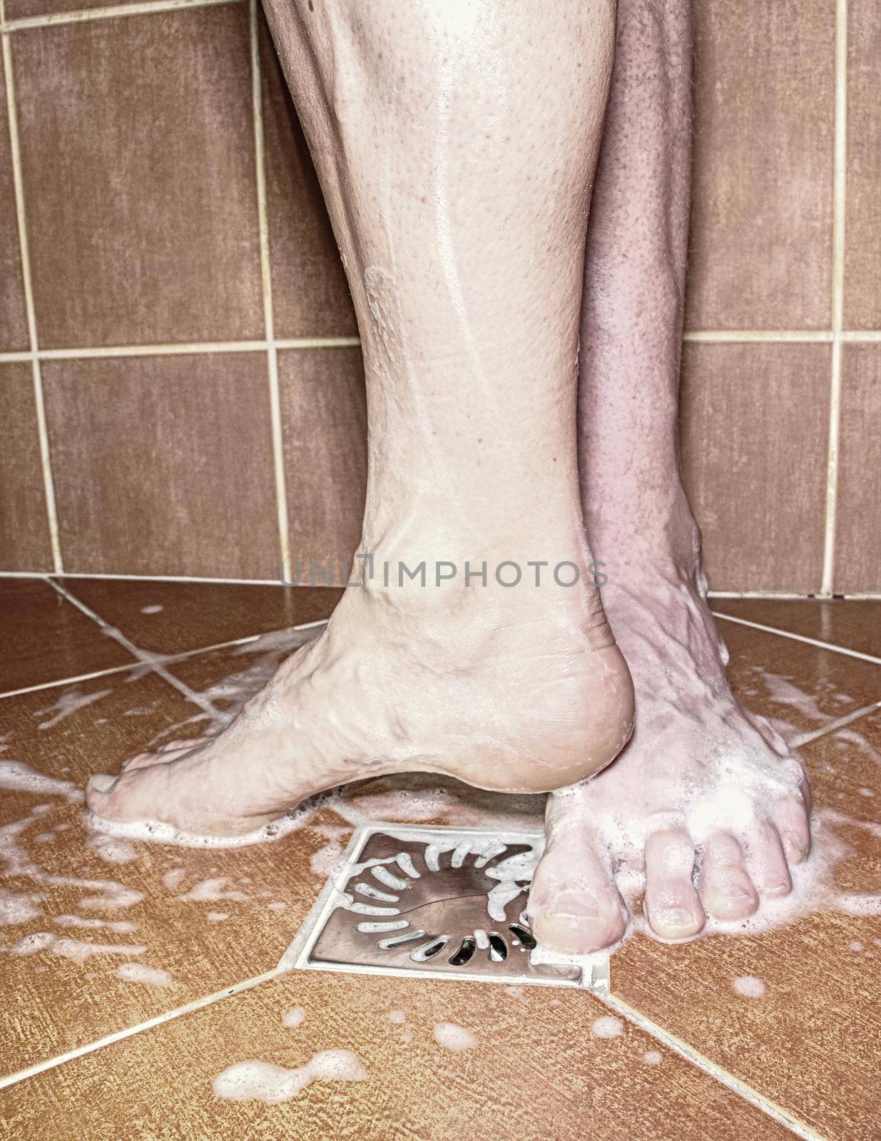 Adult couple playing in shower, naked feet on rural tilled floor. Romantic theme.