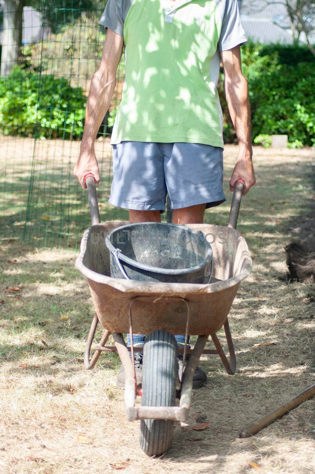 gardener man in dirty work clothes, rolls a rusty cart with a bucket, spring work in the garden. High quality photo